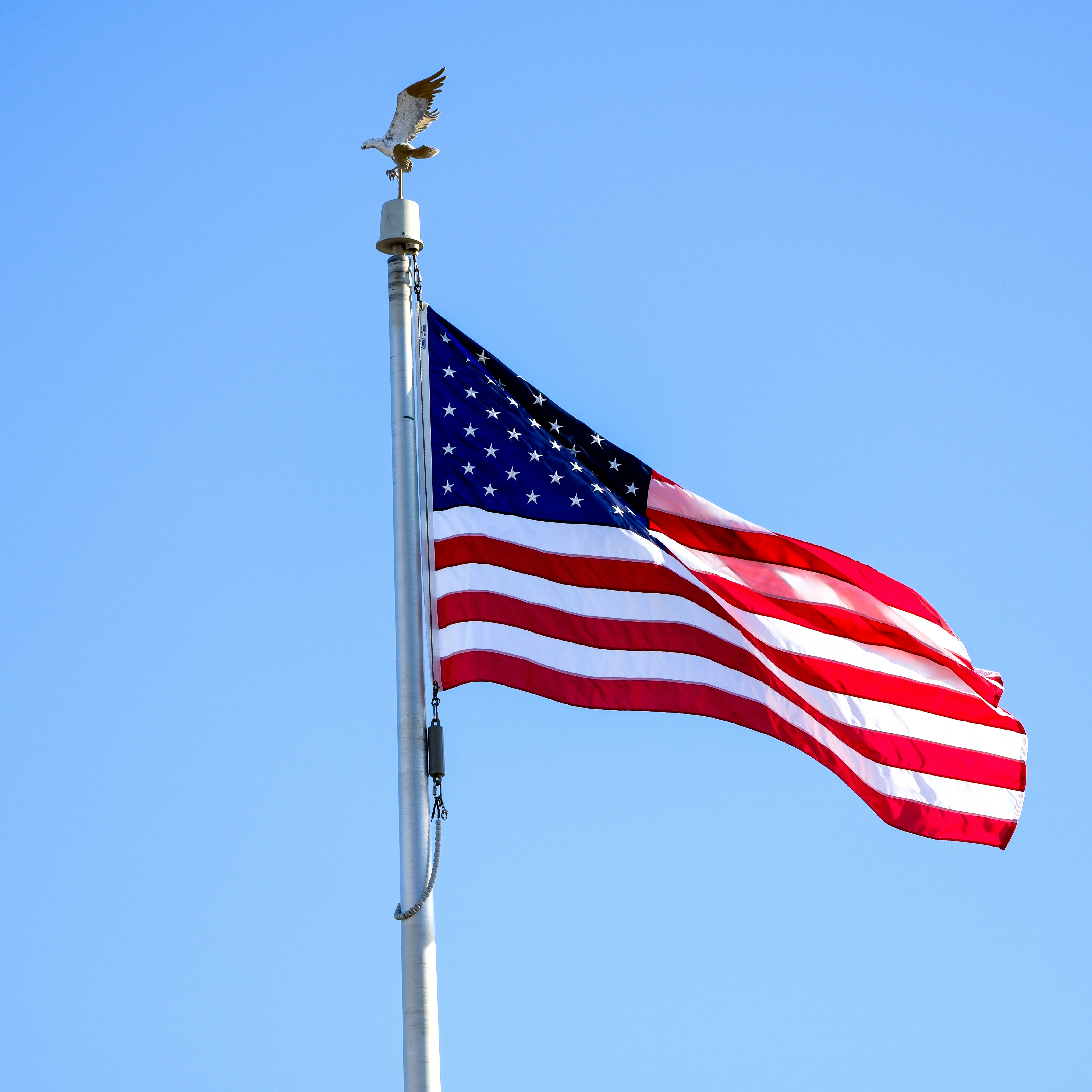 American flag waving on a flagpole against blue sky.