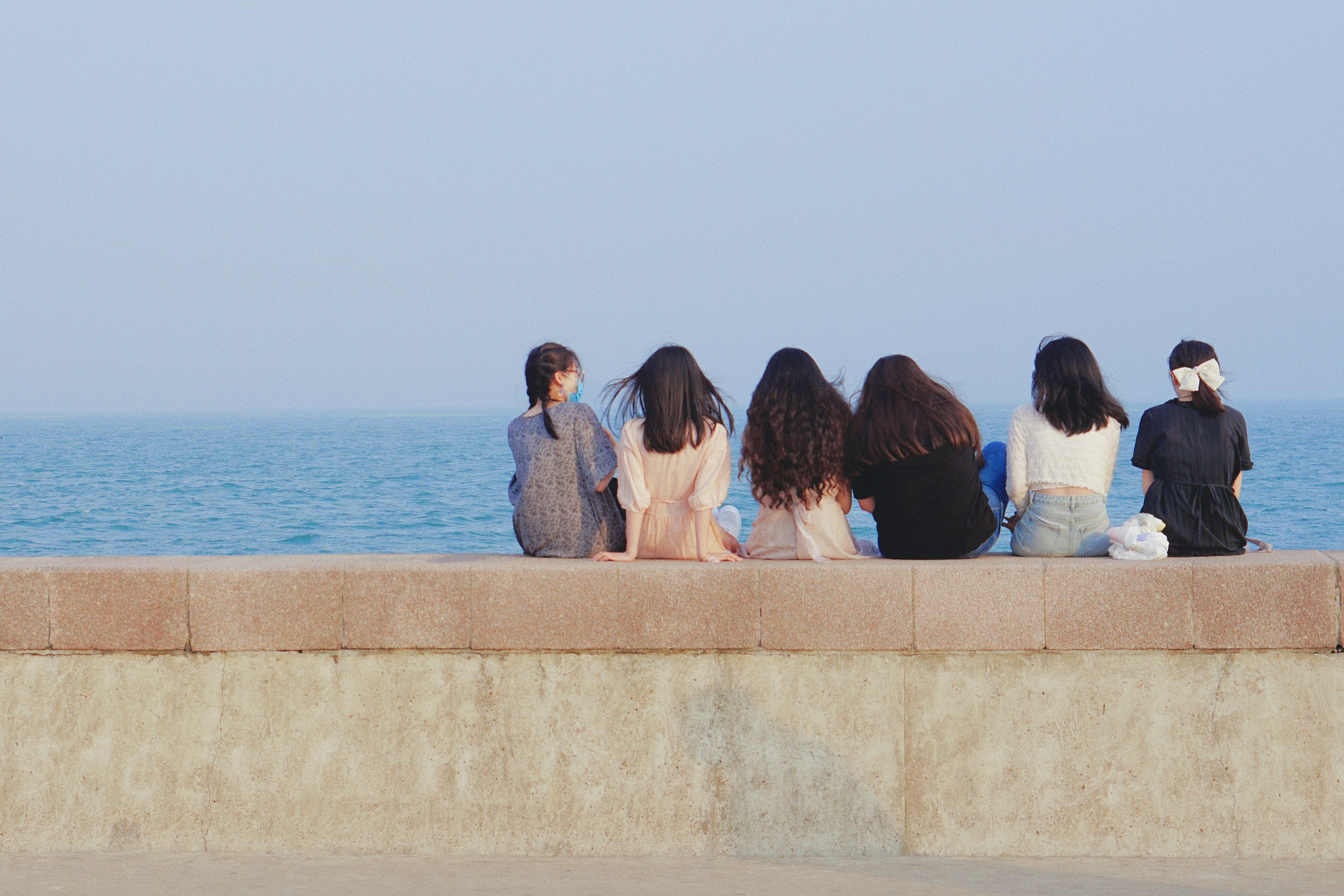 Six friends sitting on a wall by the ocean