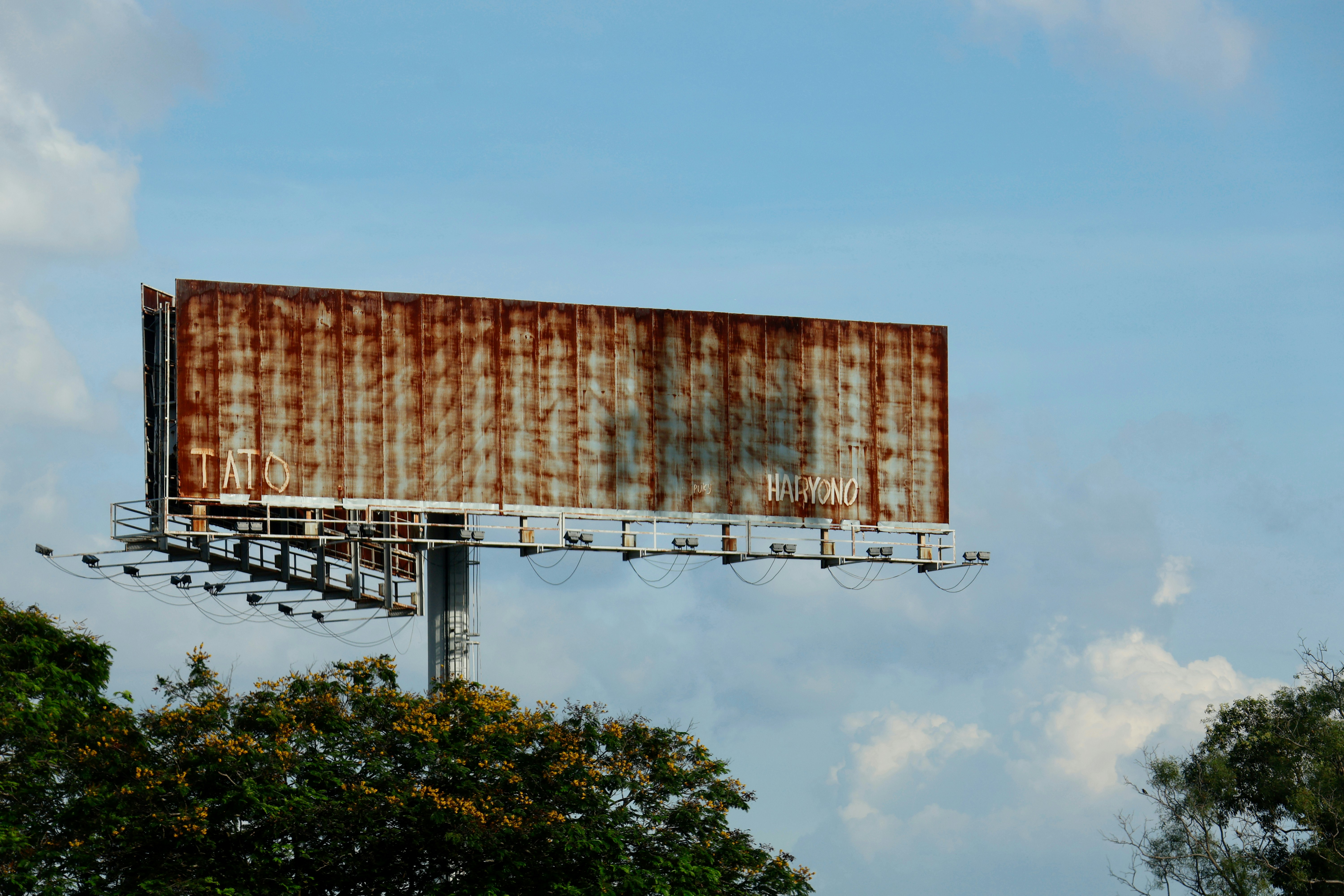 An old, rusty billboard against a cloudy sky.