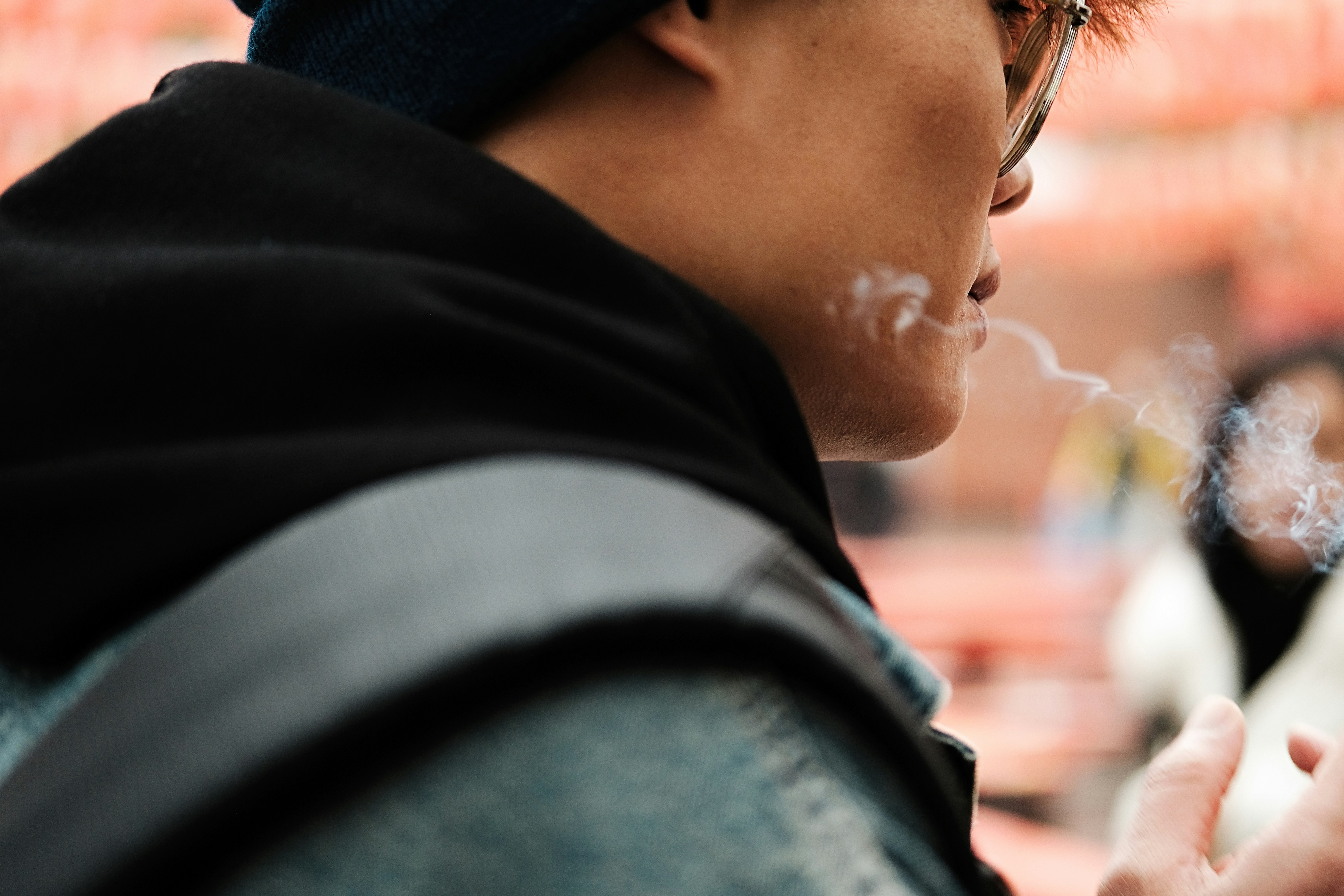 A person exhales smoke, wearing a hoodie and beanie.