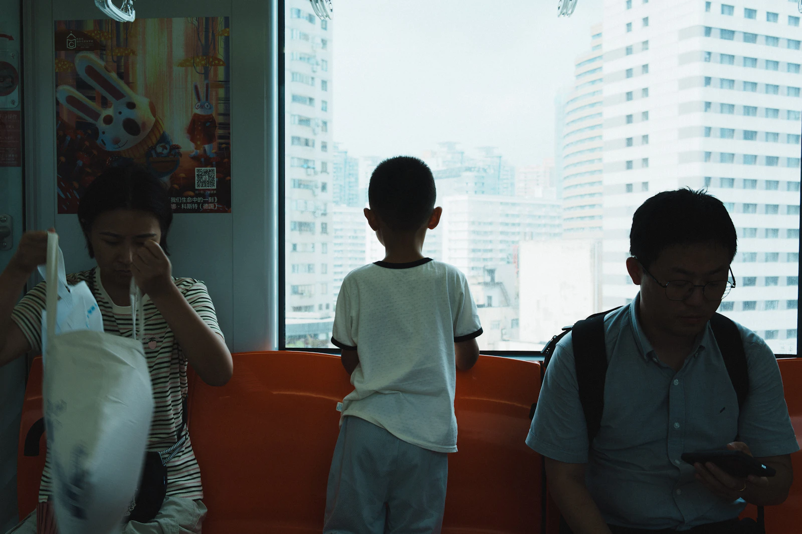 Passengers look through train windows as tall city buildings come into view.