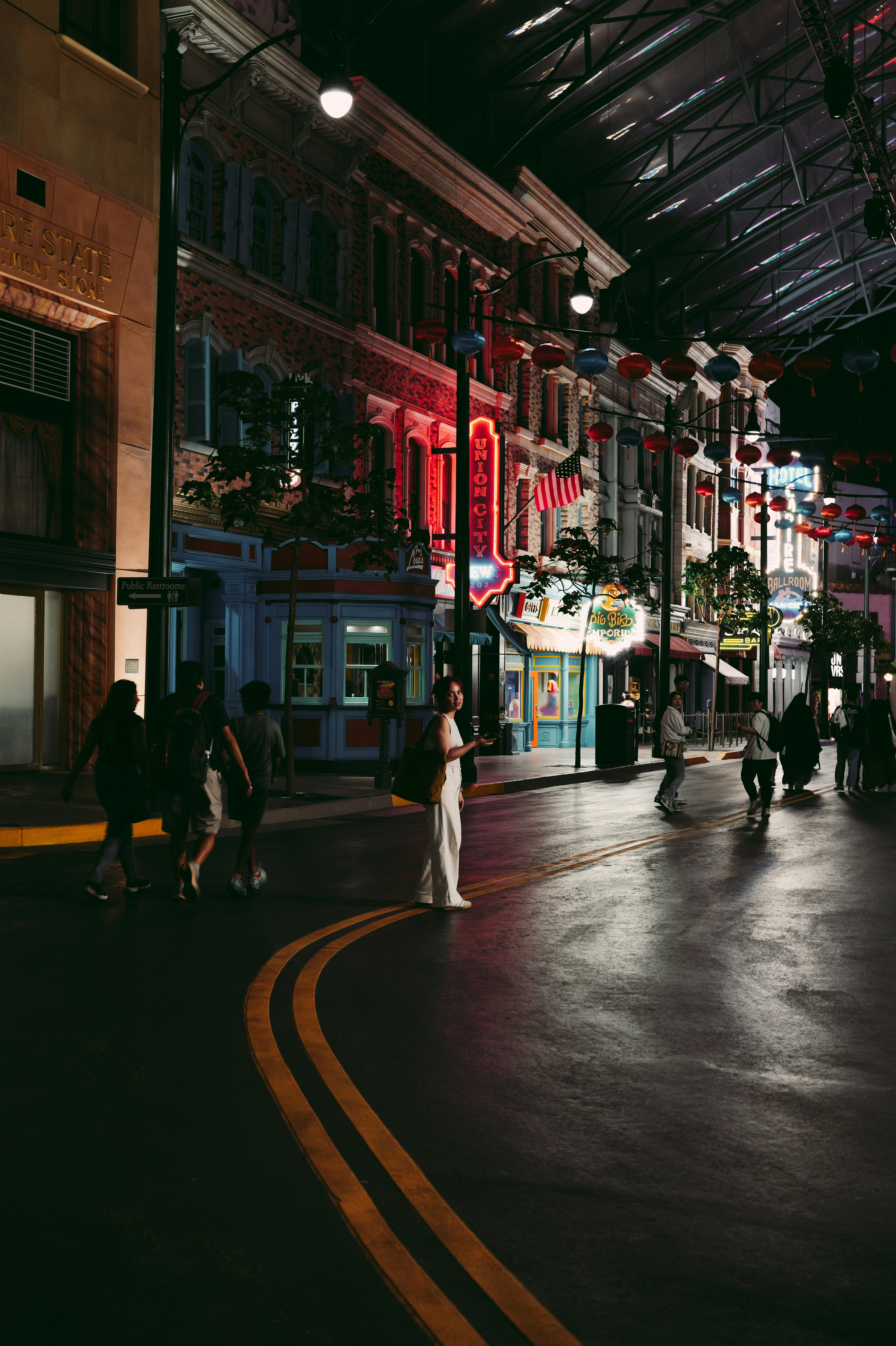 People walk down a street with illuminated buildings at night.