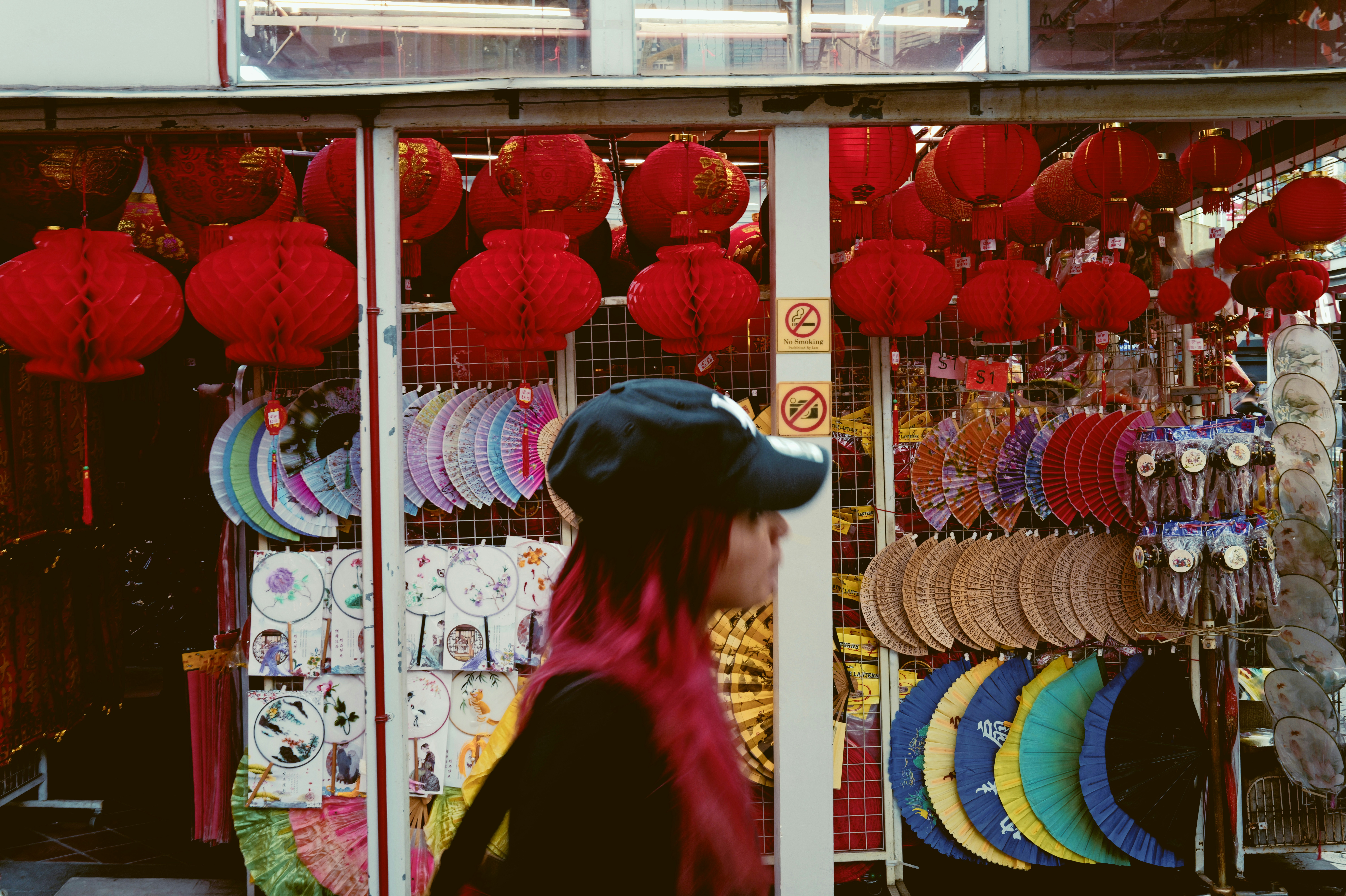 Woman with pink hair walks past a stall with lanterns.