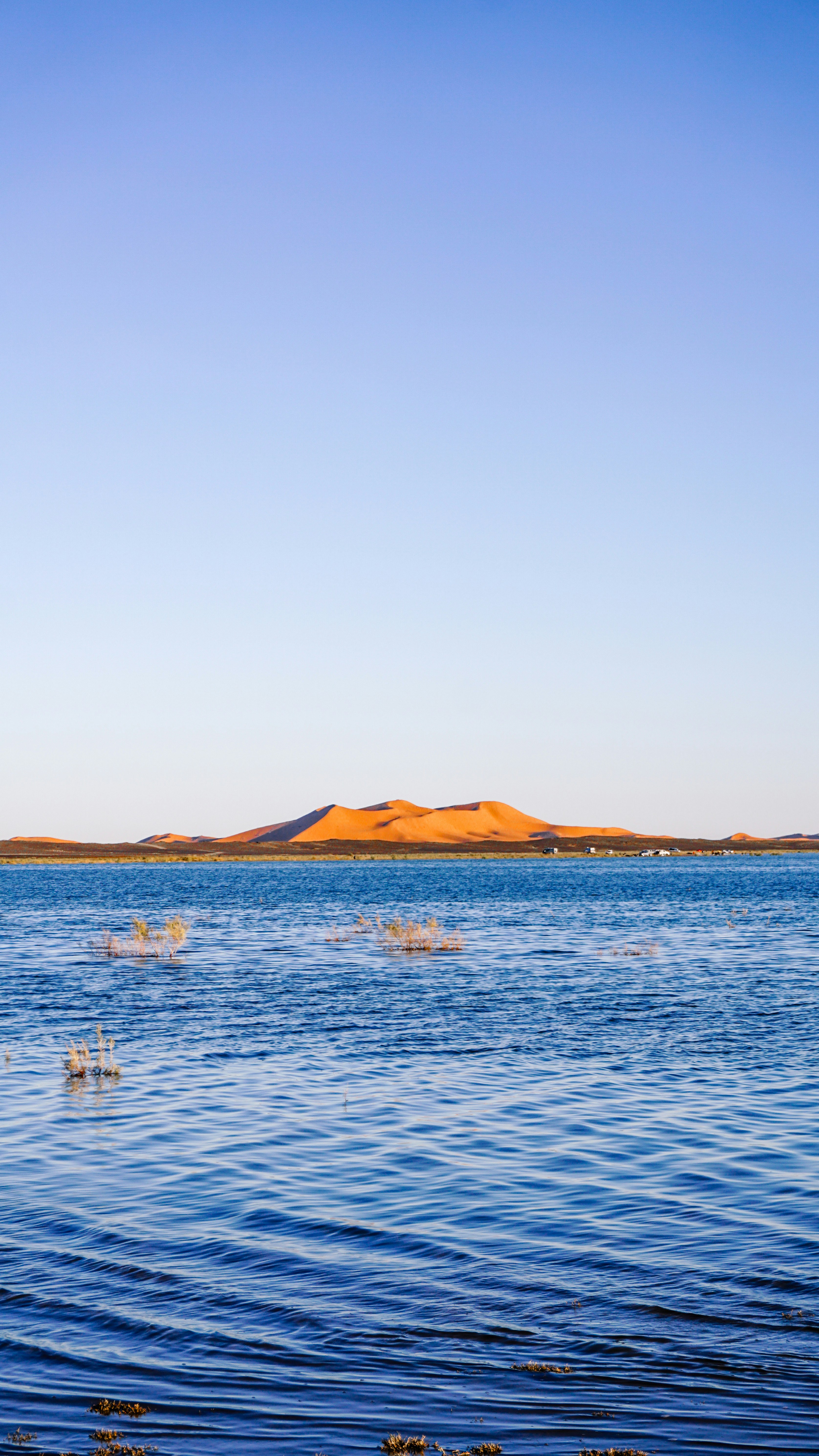 Golden hills rise above a calm blue lake at sunset.