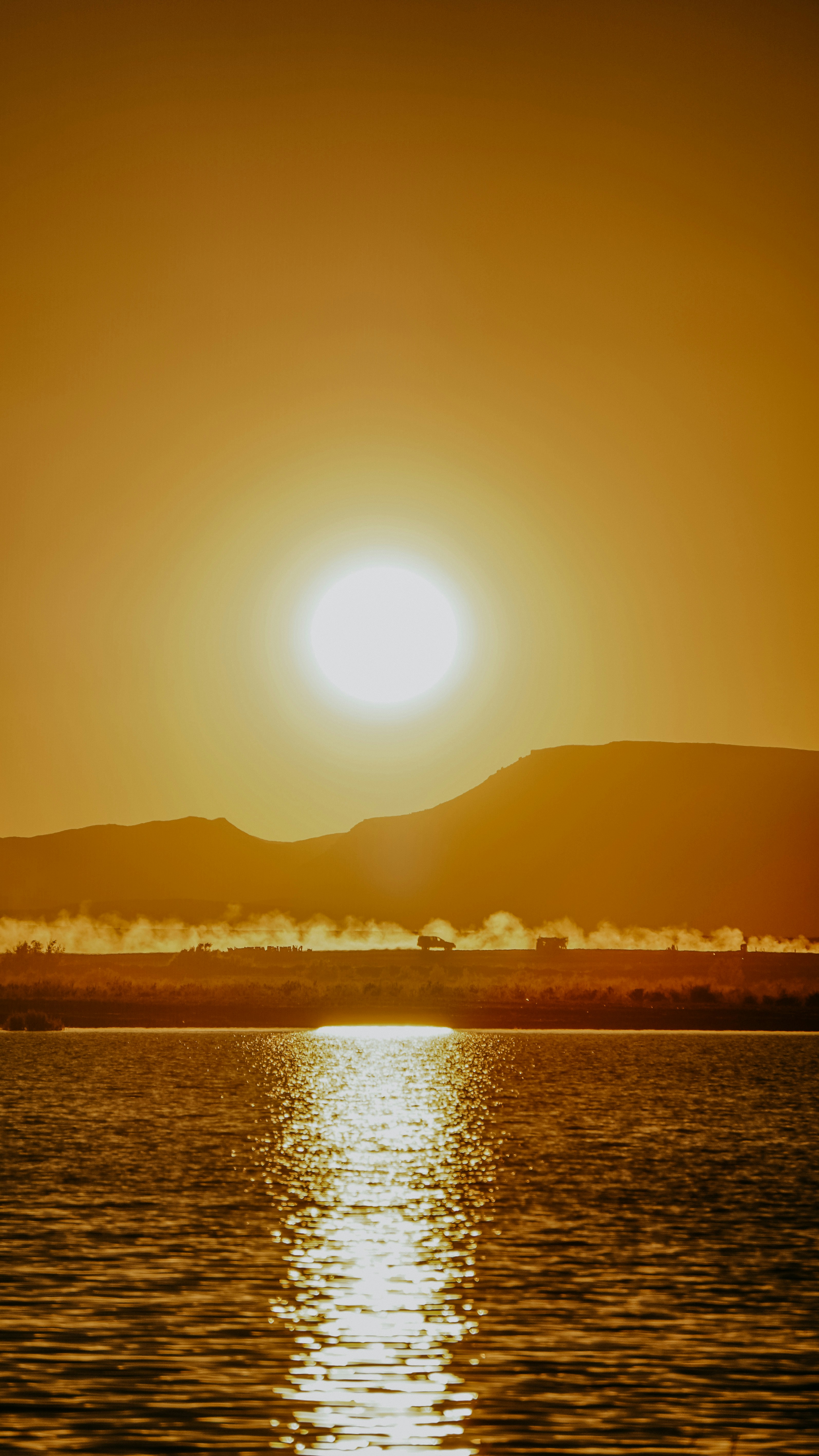 Sunset over a calm lake with distant mountains.