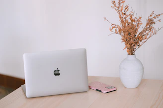 Laptop, phone, and dried flowers on a wooden desk.