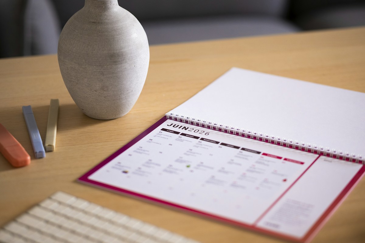 A calendar and vase on a wooden desk, illustrating online appointment scheduling for schools and groups.