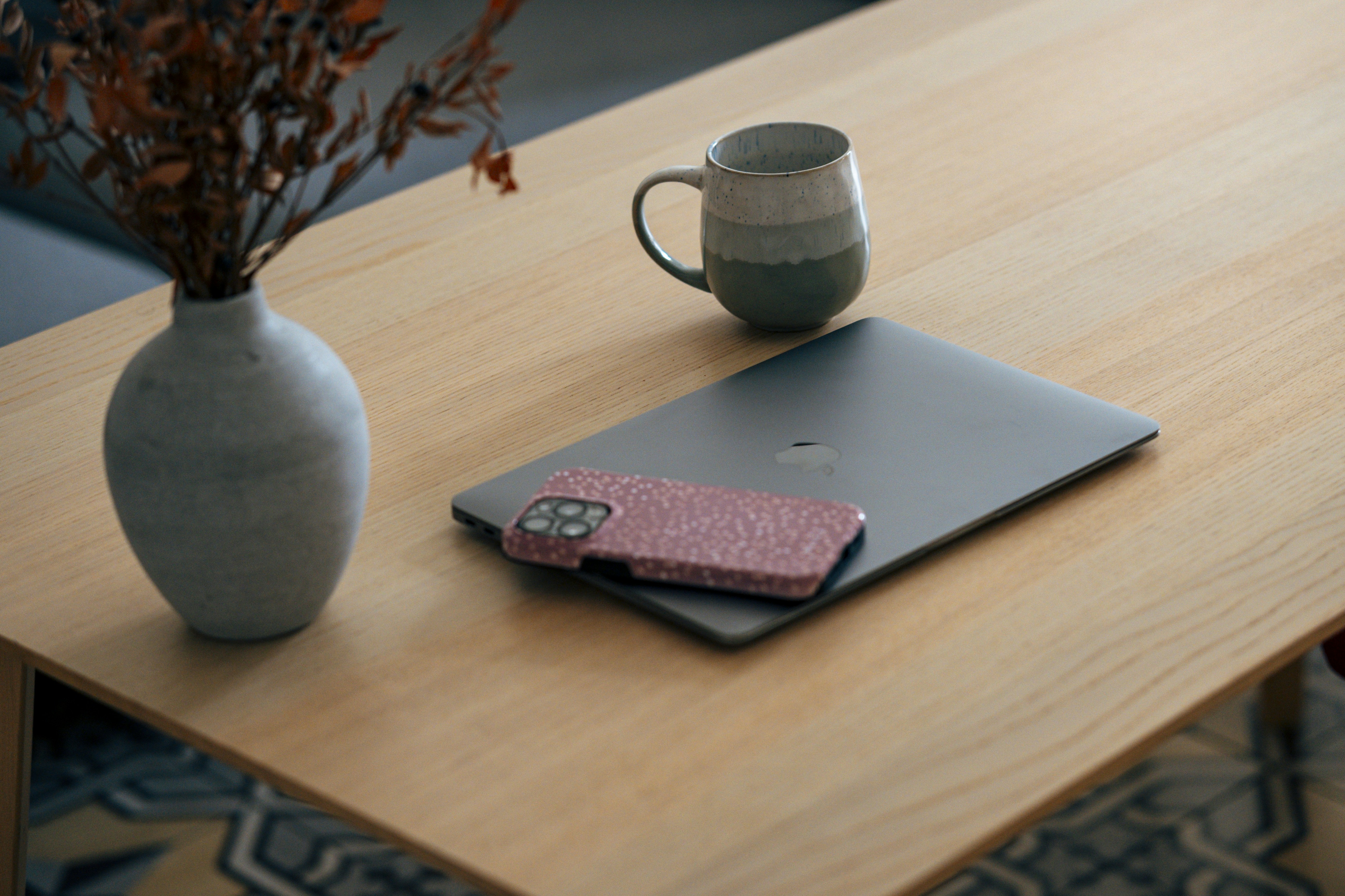 Laptop, phone, and mug on a wooden table.