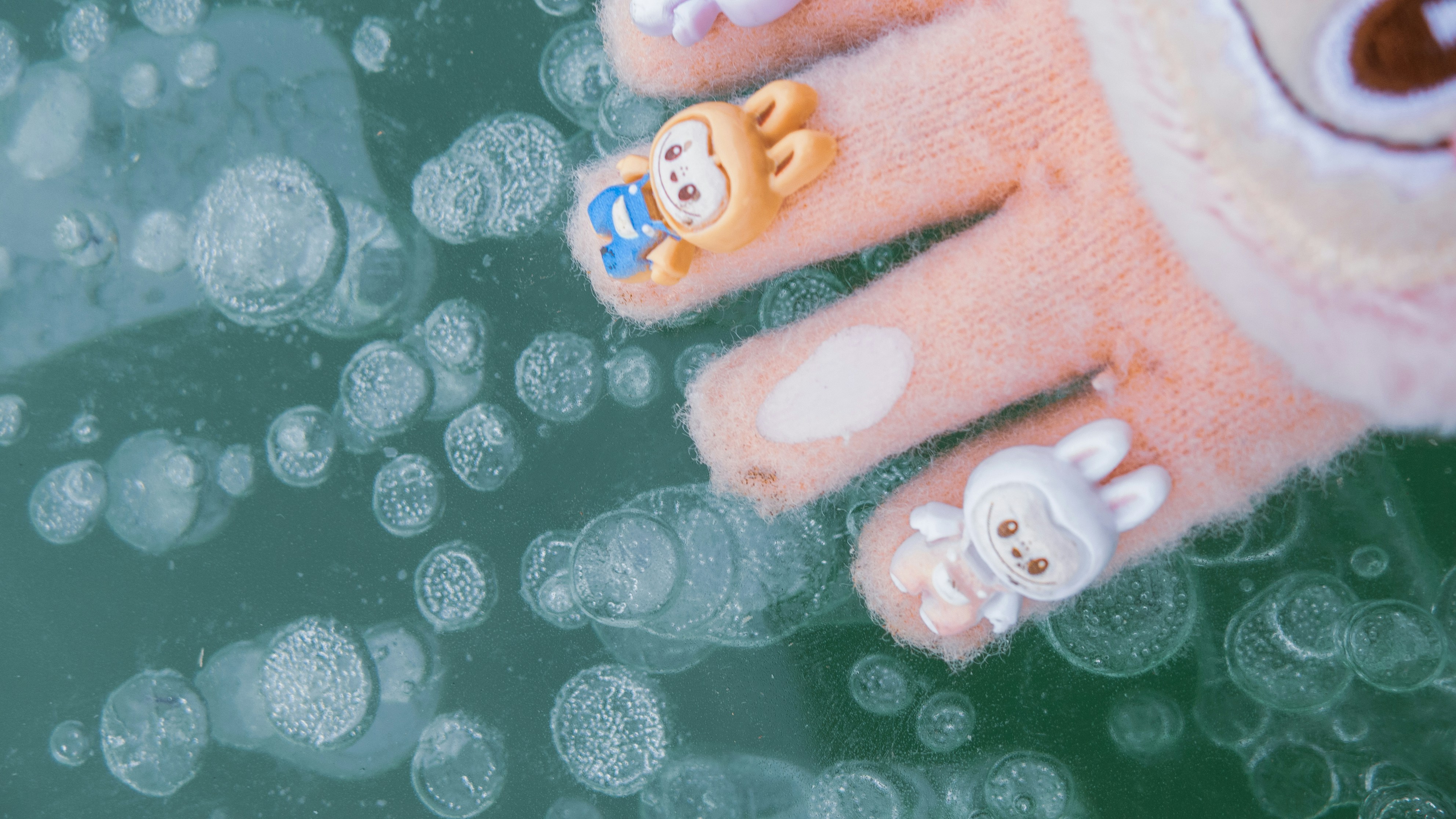 Child's gloved hand with bunny charms touches frozen bubbles.