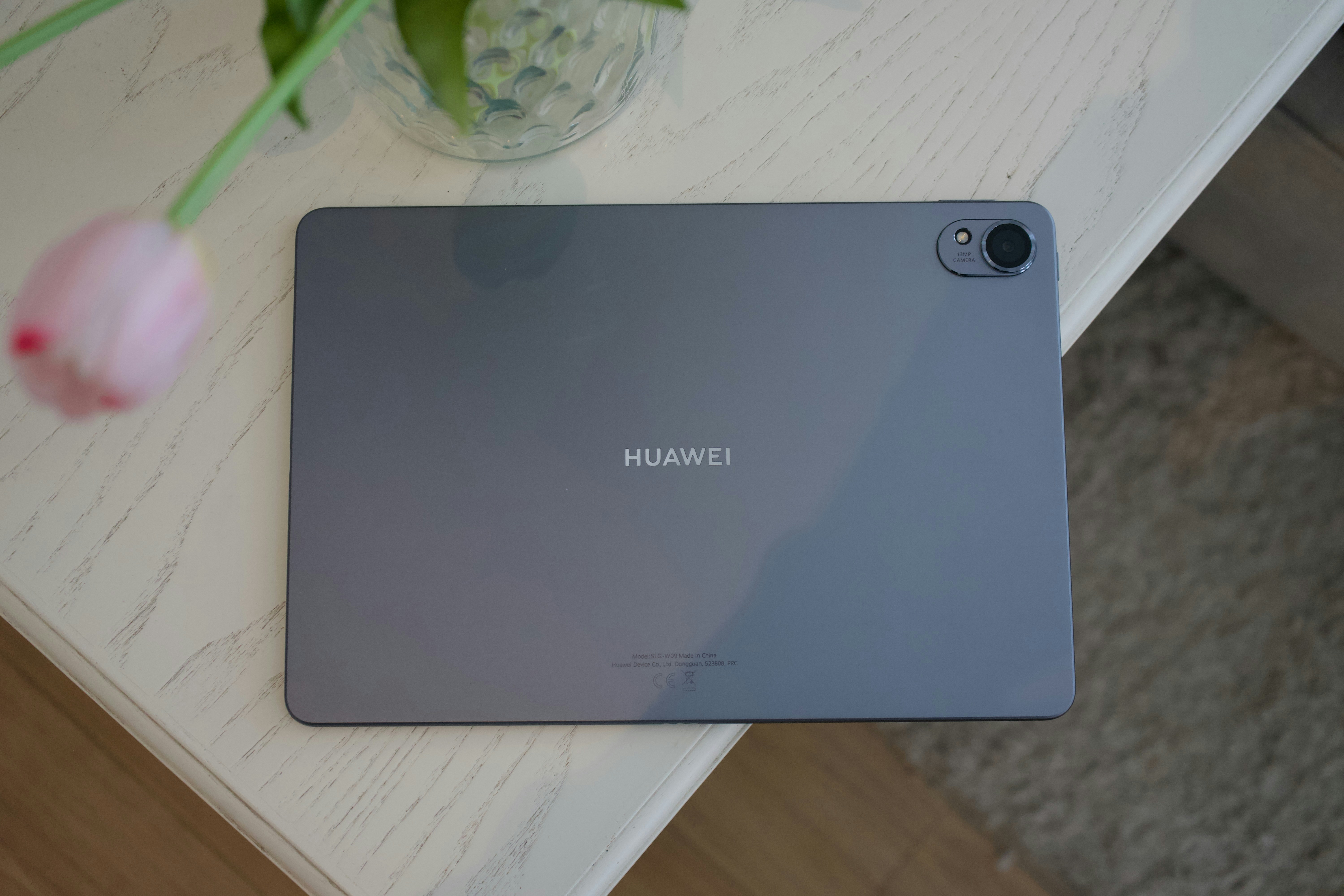 Tablette Huawei grise sur une table blanche avec une fleur