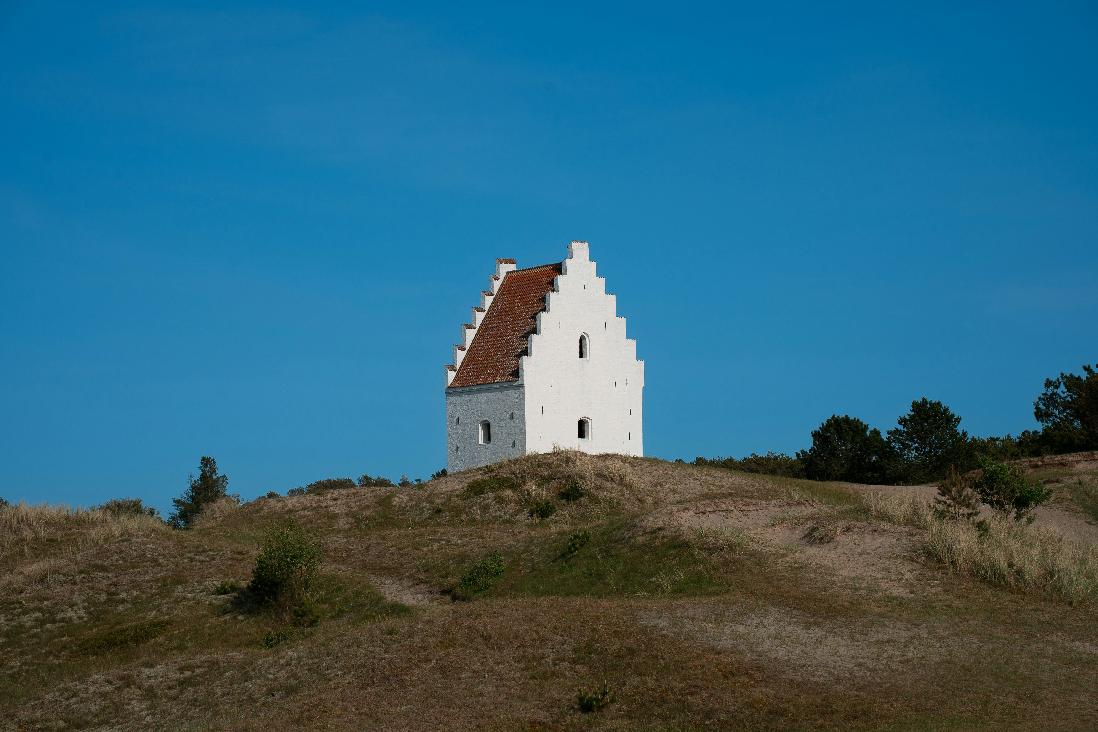 White building with red roof on grassy hill