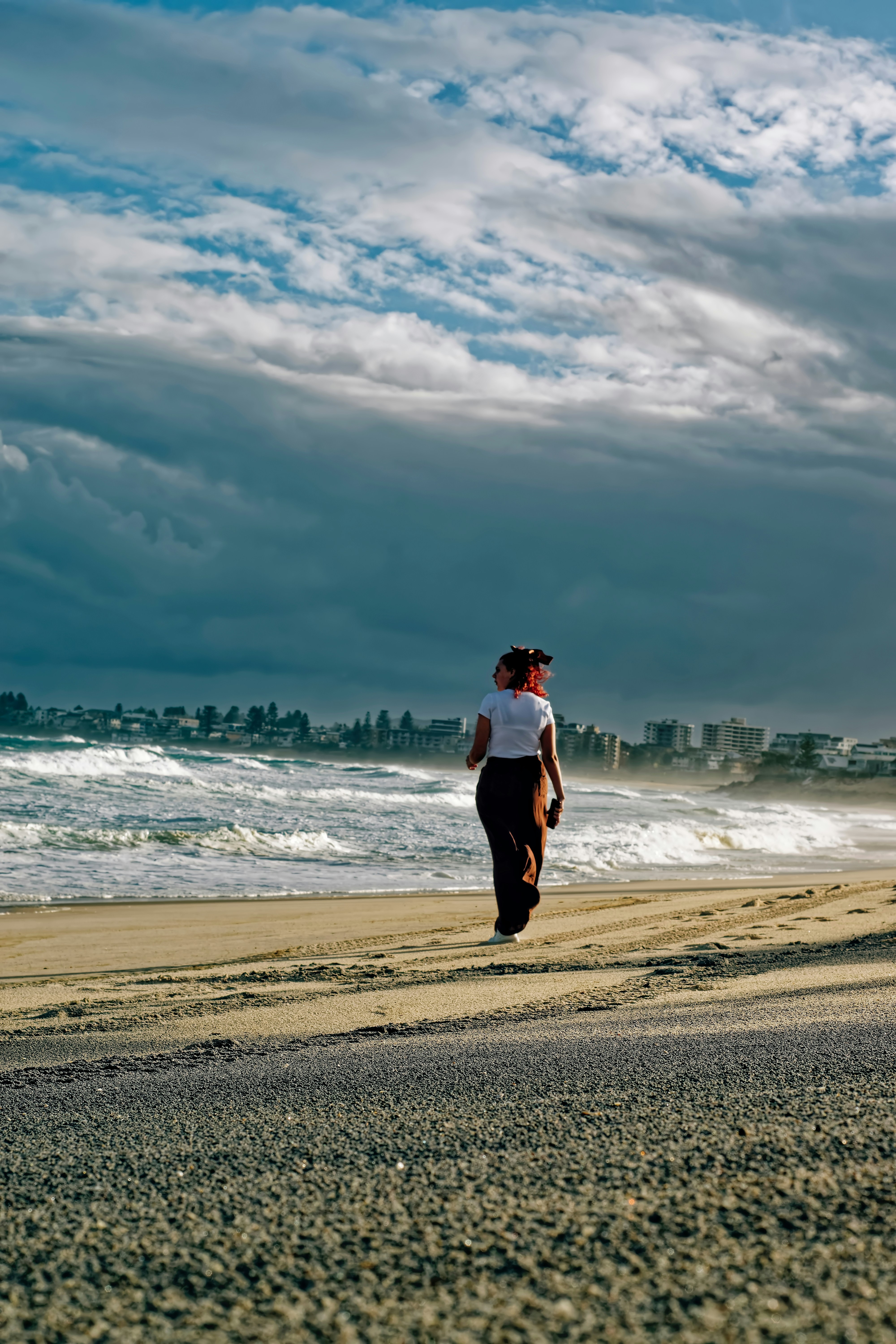 Donna cammina sulla spiaggia con lo skyline della città lontano