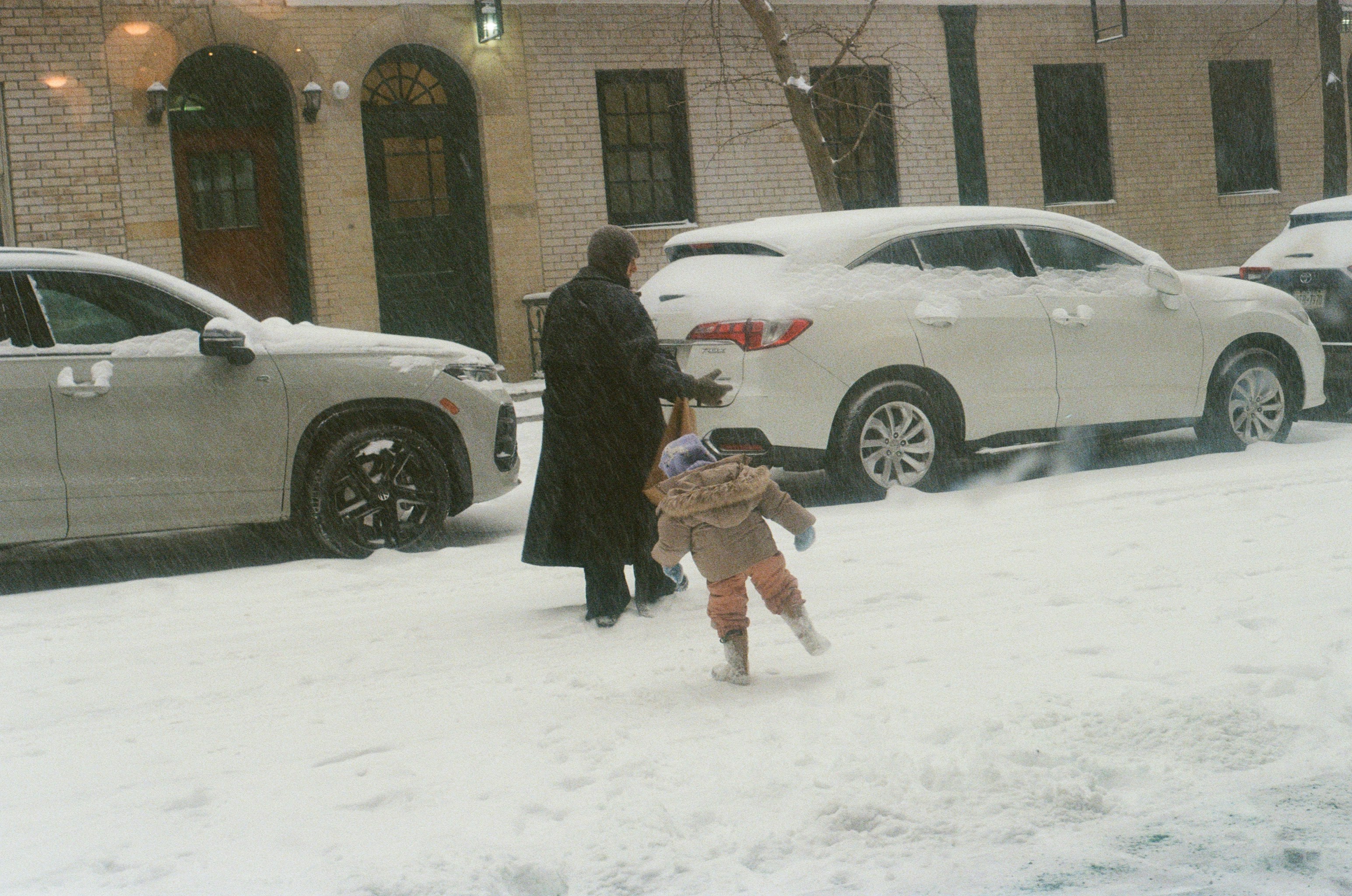 Adult and child walking in a snowy street.