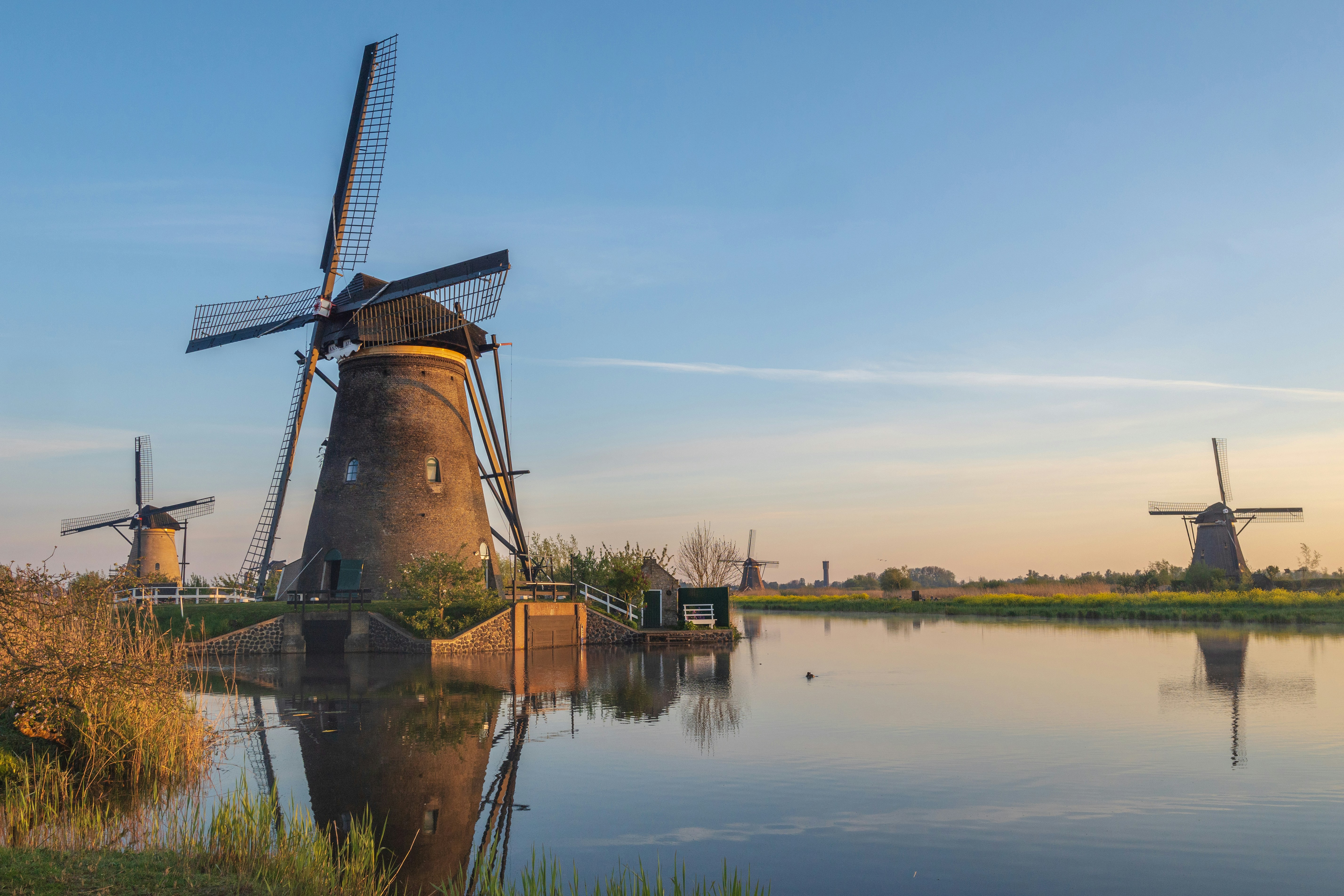 Historic windmills stand beside a calm canal at sunset.
