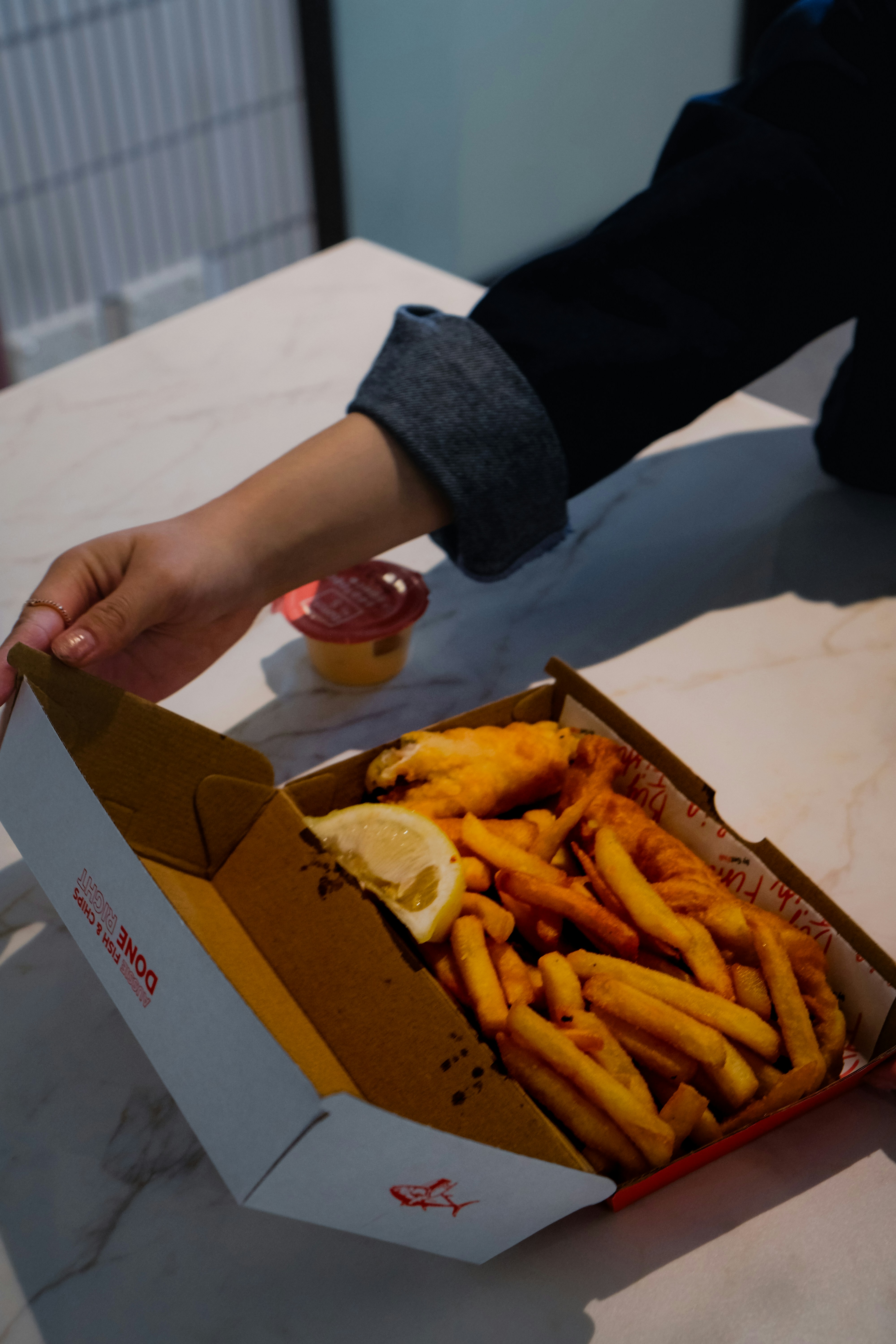 Hand opening box of fish and chips with lemon