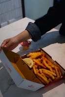 Hand opening box of fish and chips with lemon