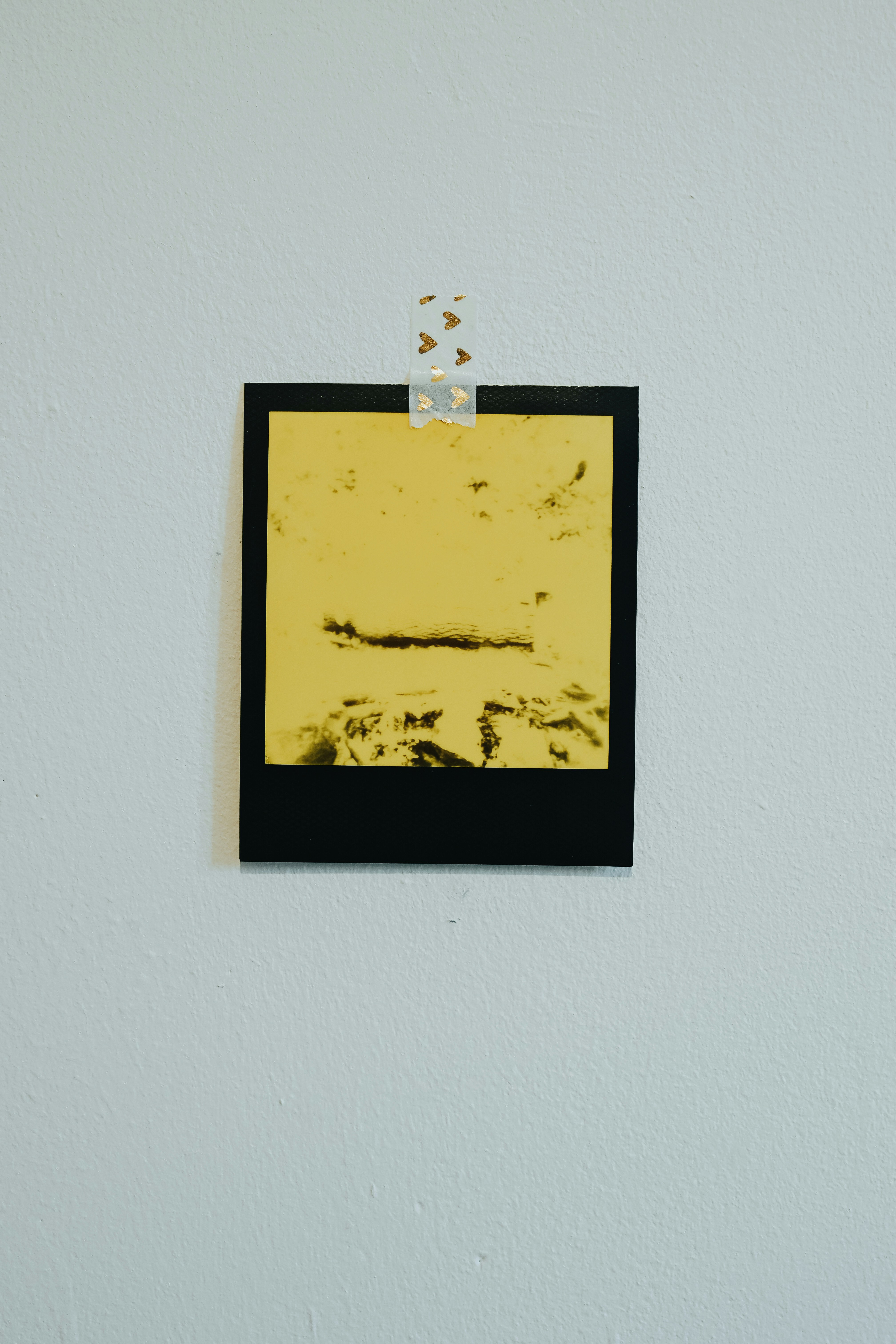 A yellow abstract artwork taped to a white wall.