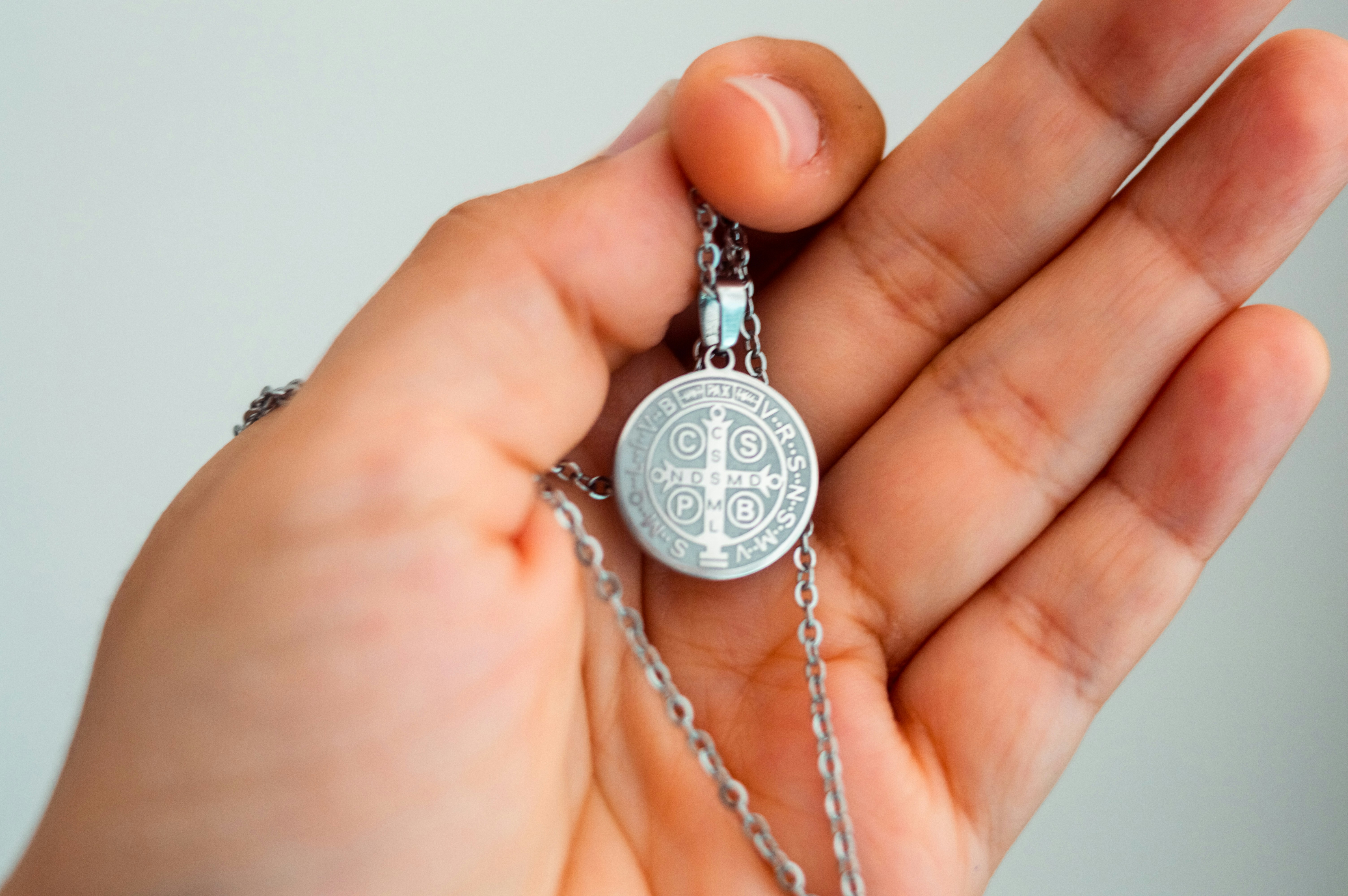 Hand holding a silver st. benedict medal necklace