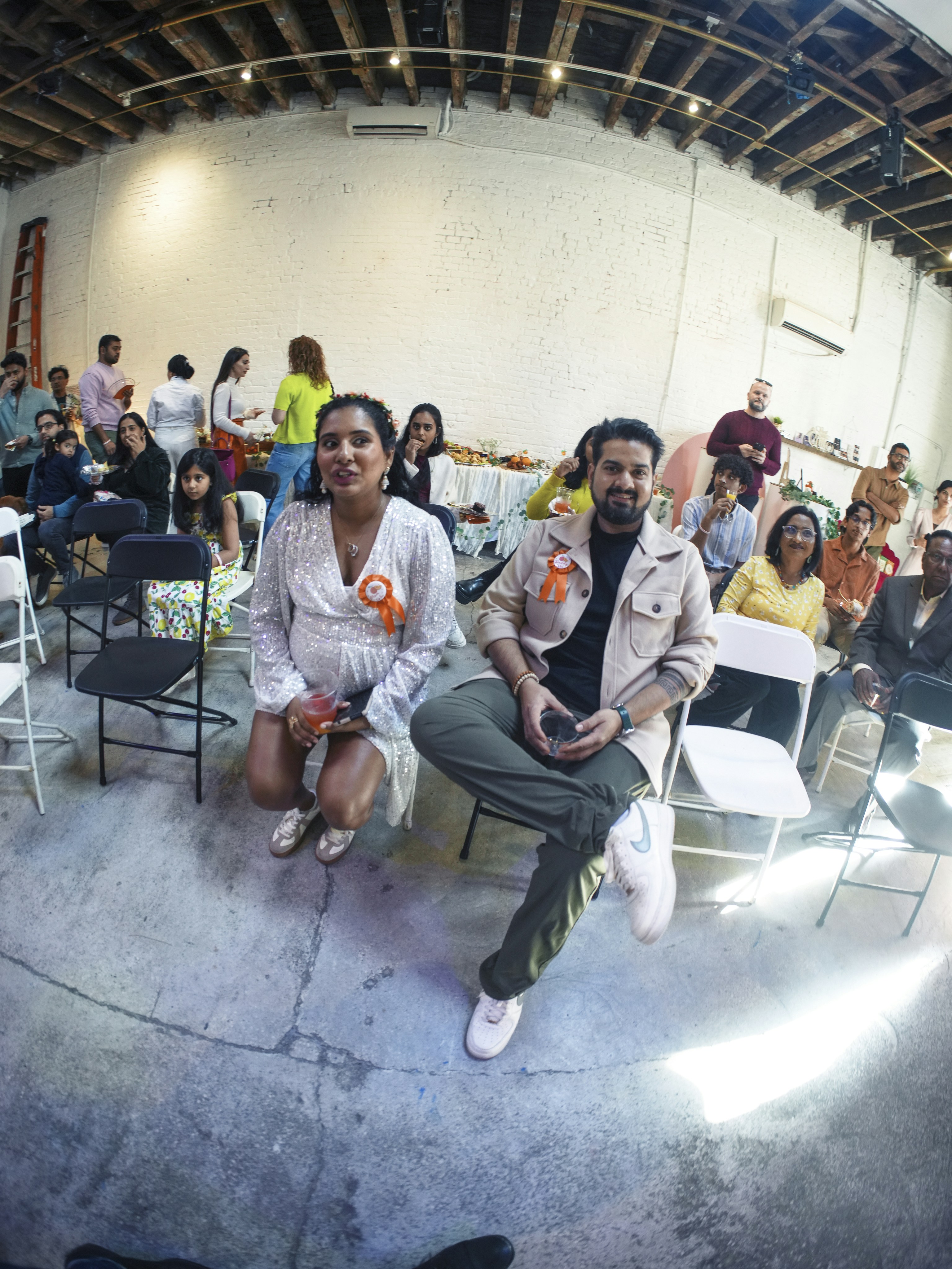A couple sits in chairs at an event with guests.