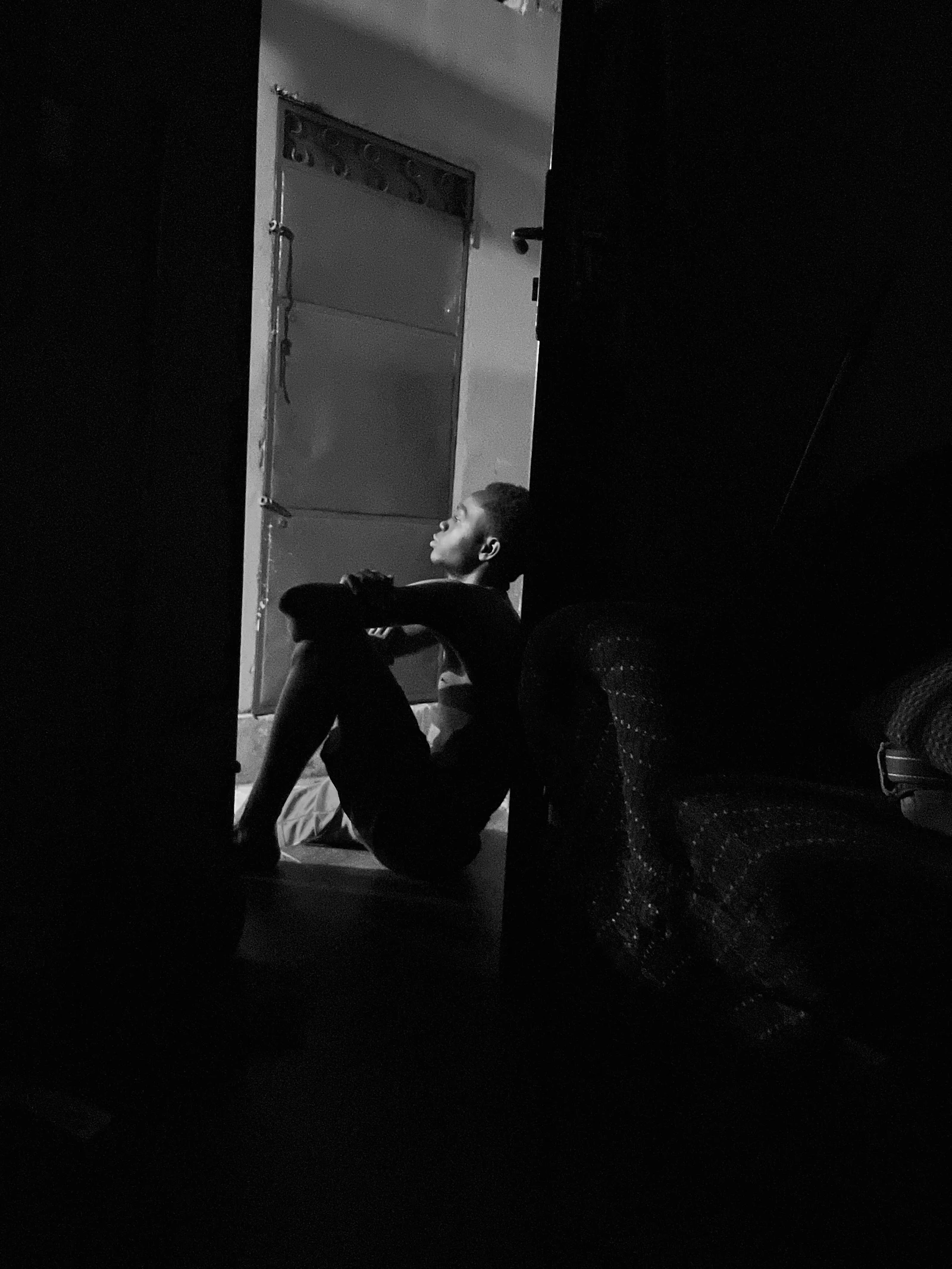 Person sitting alone in a dark doorway during a quiet moment of emotional withdrawal