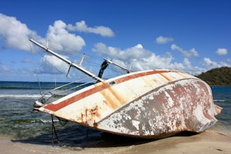 A wrecked sailboat lies on a sandy beach.