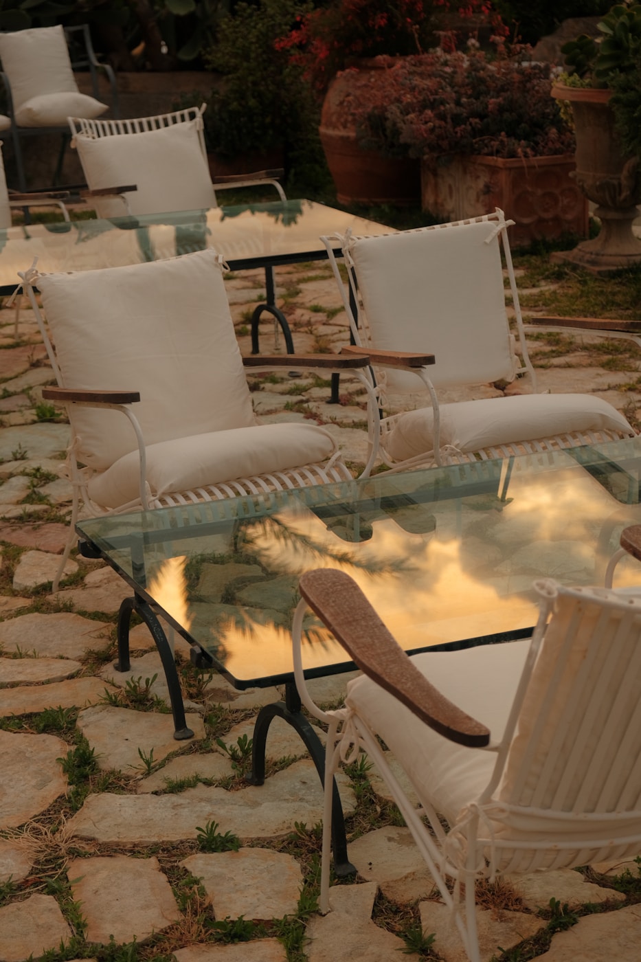 Outdoor seating area with white cushioned chairs and glass tables arranged on a stone patio