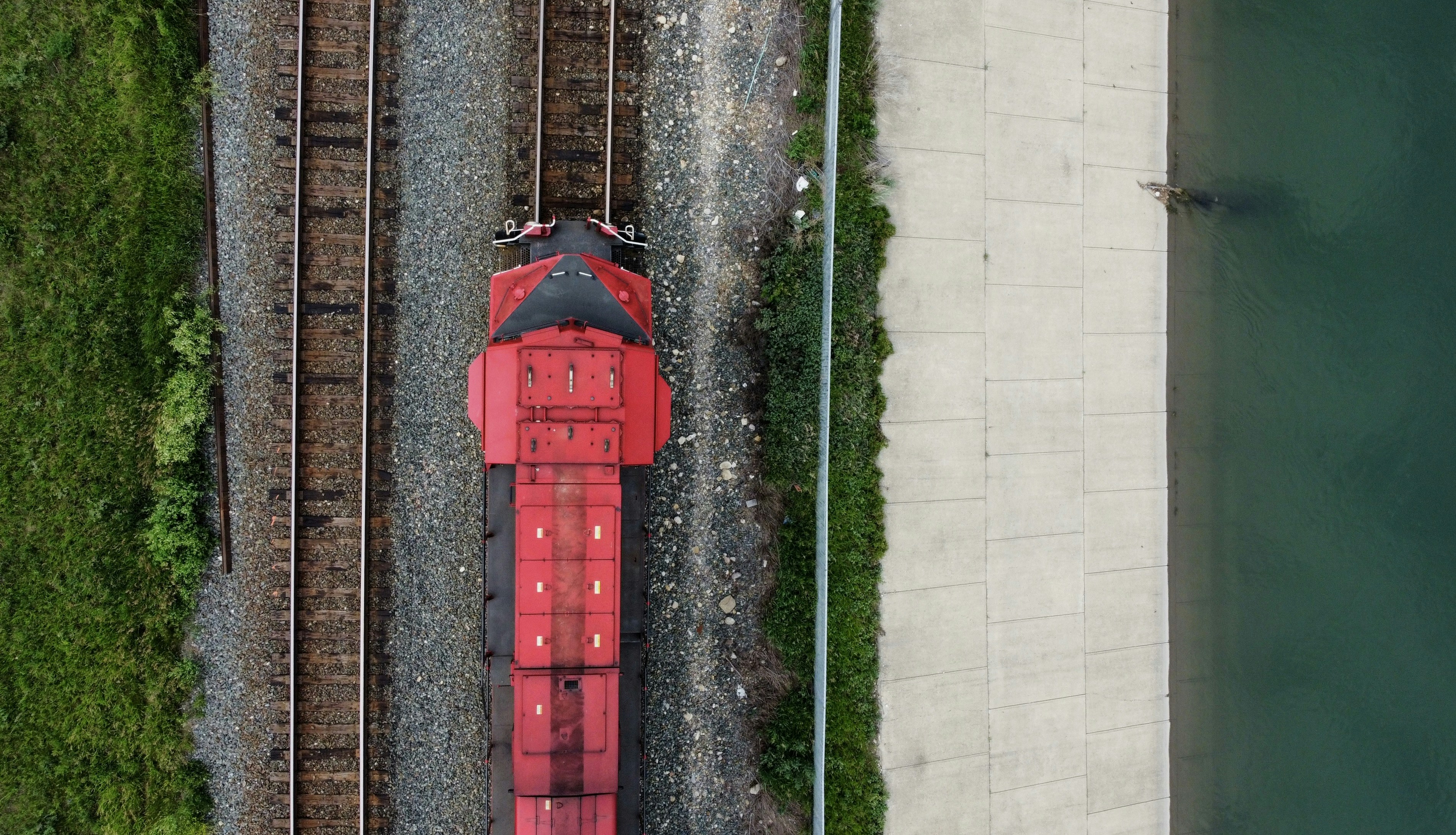 Red train on tracks beside water and greenery