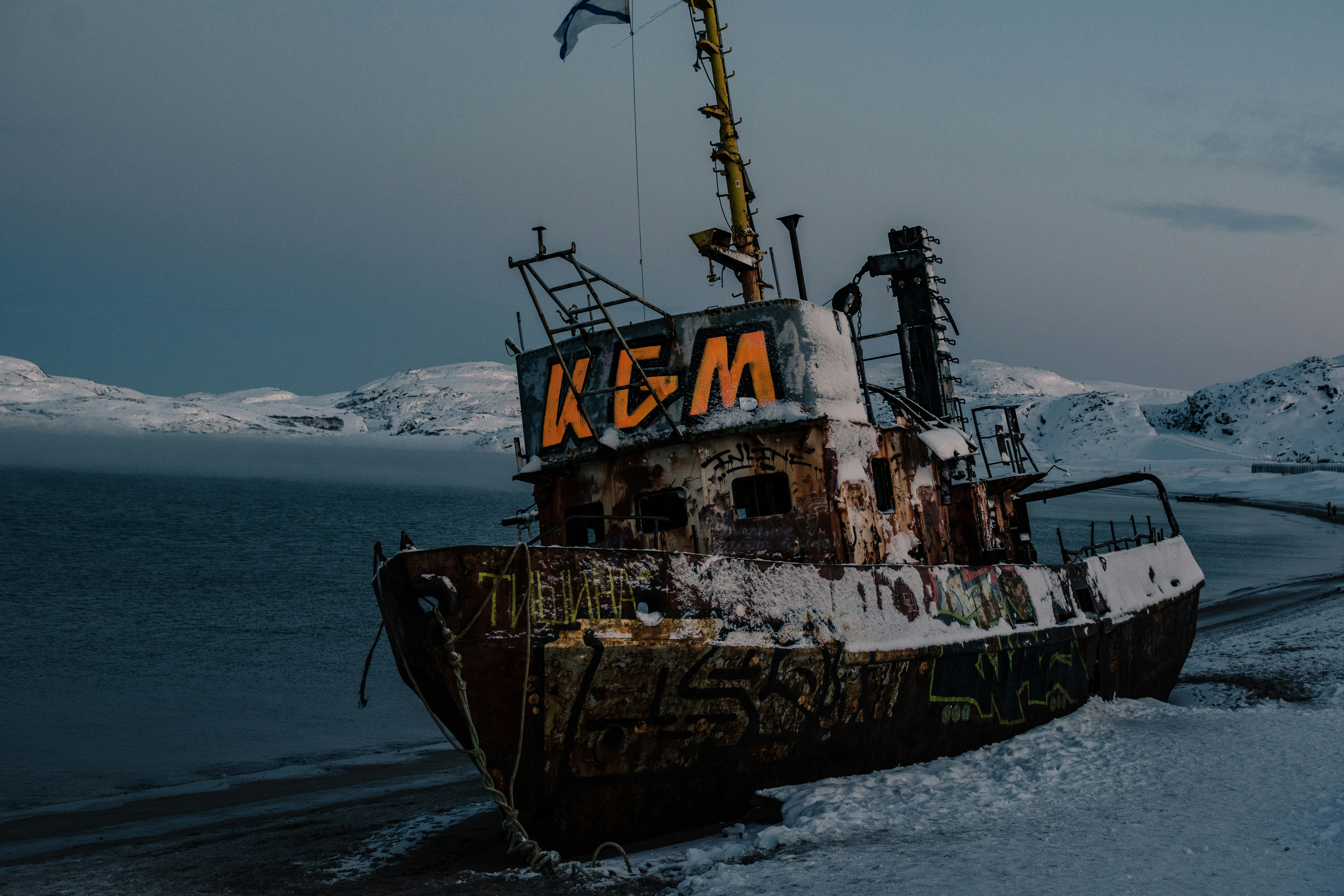 Um velho naufrágio enferrujado repousa em uma costa nevada.