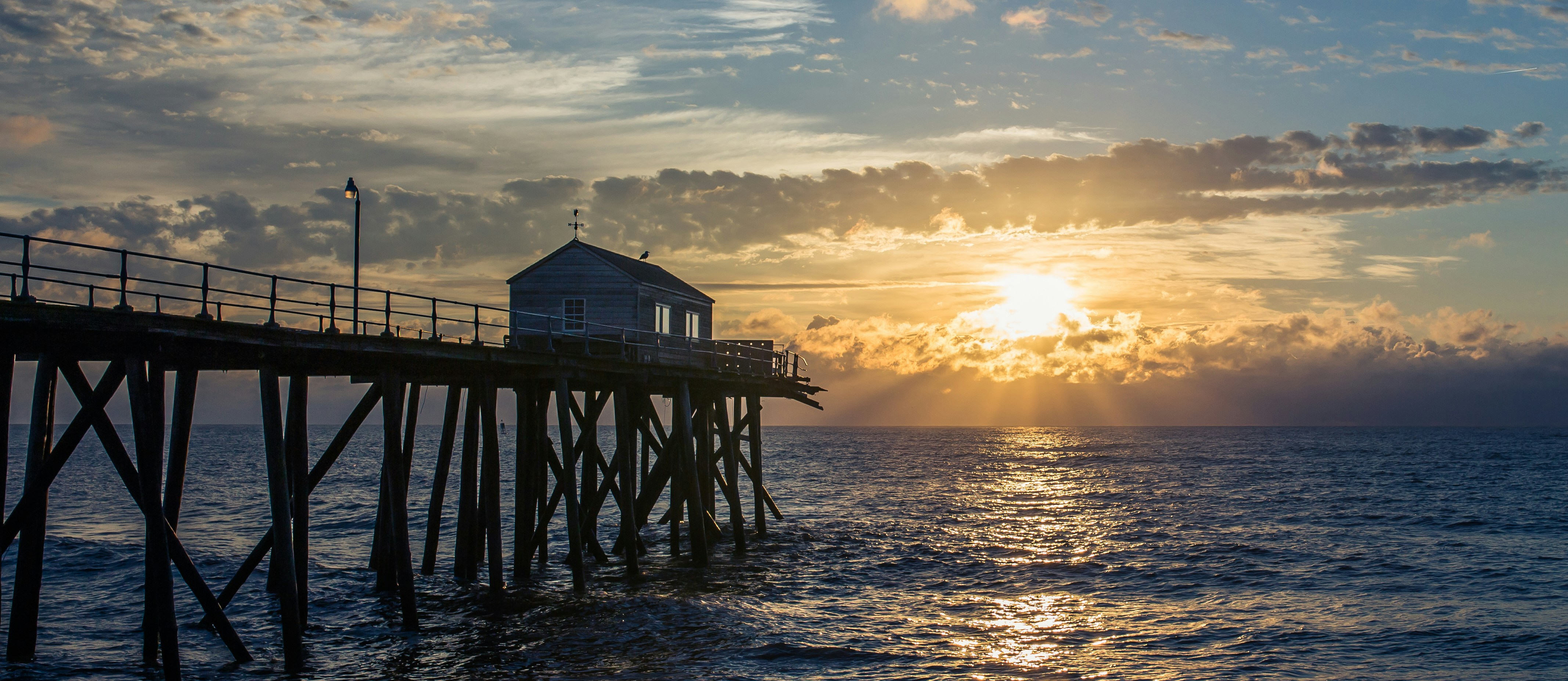 Pier with a small building over the ocean at sunset.