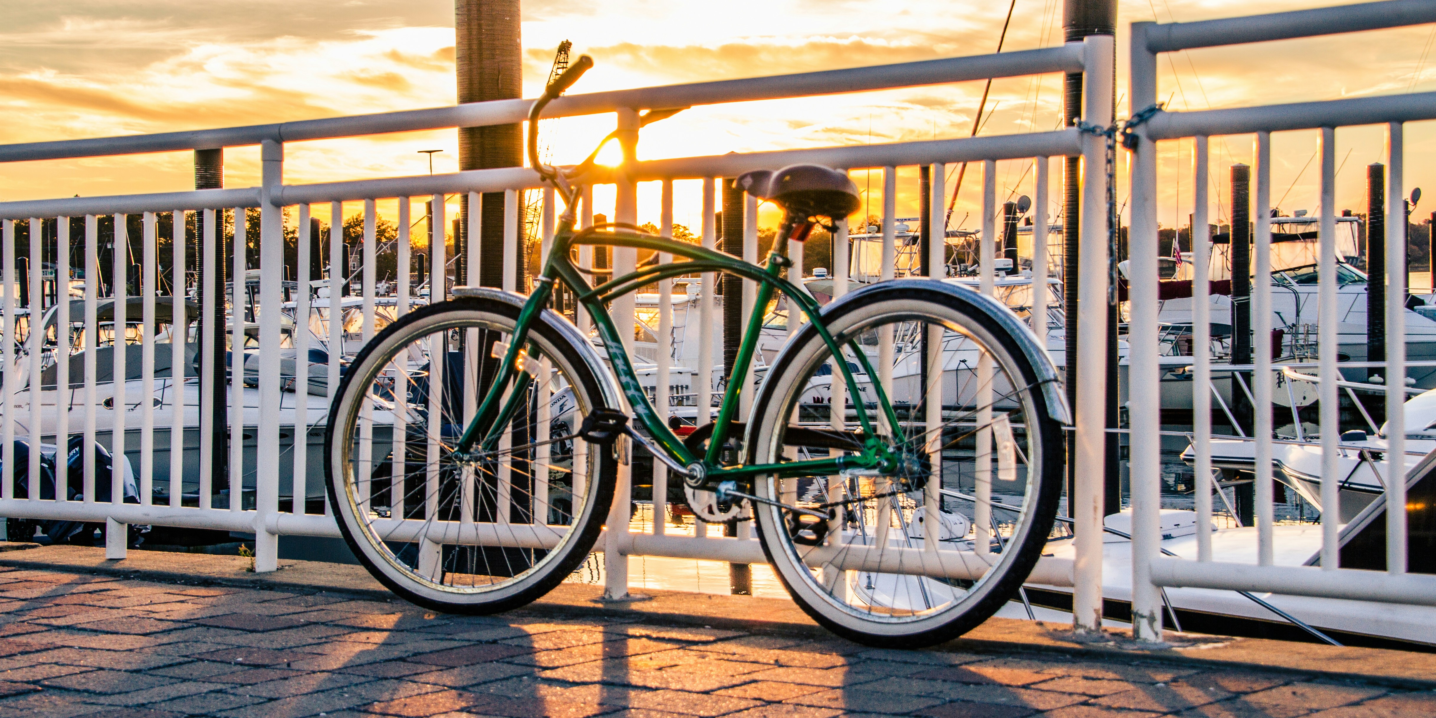 A green bicycle rests by a railing at sunset.
