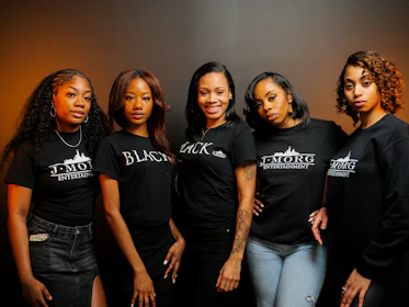 Five women posing together wearing black t-shirts.