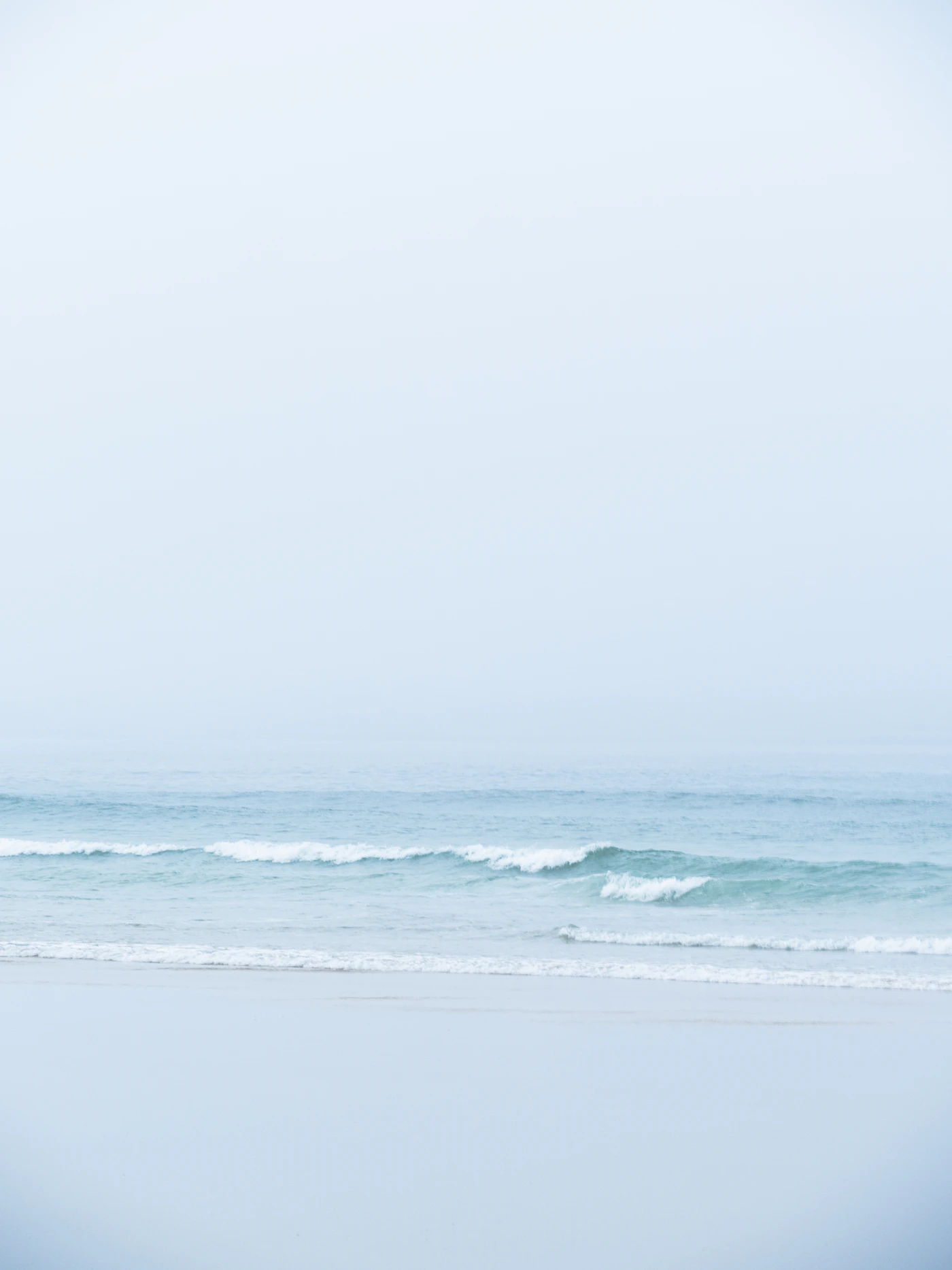 Calm waves rolling onto a pale, misty shore