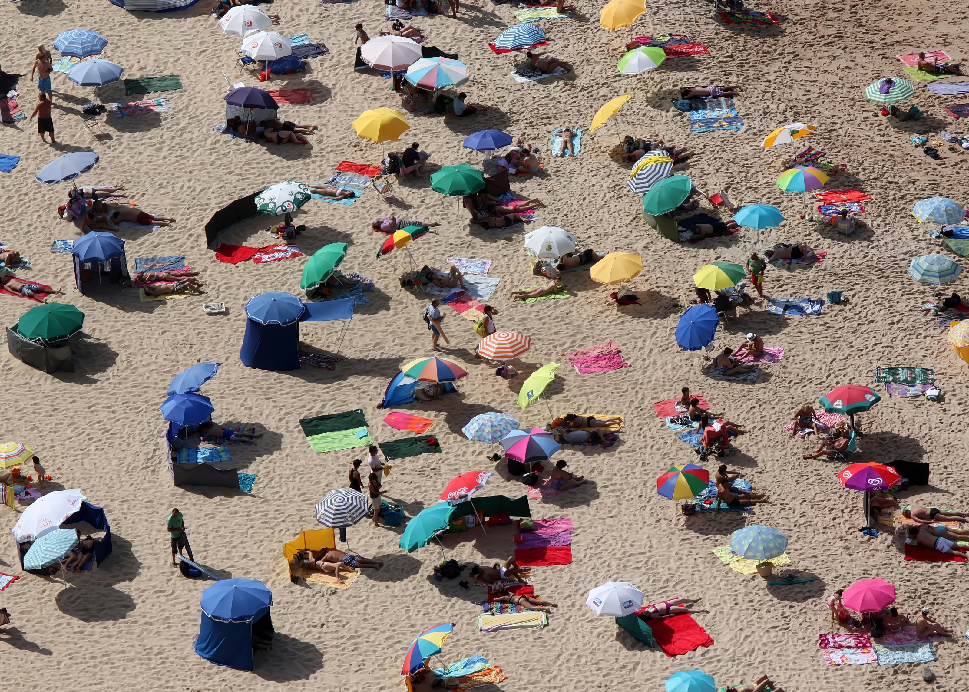 Crowded beach with many colorful umbrellas and people.