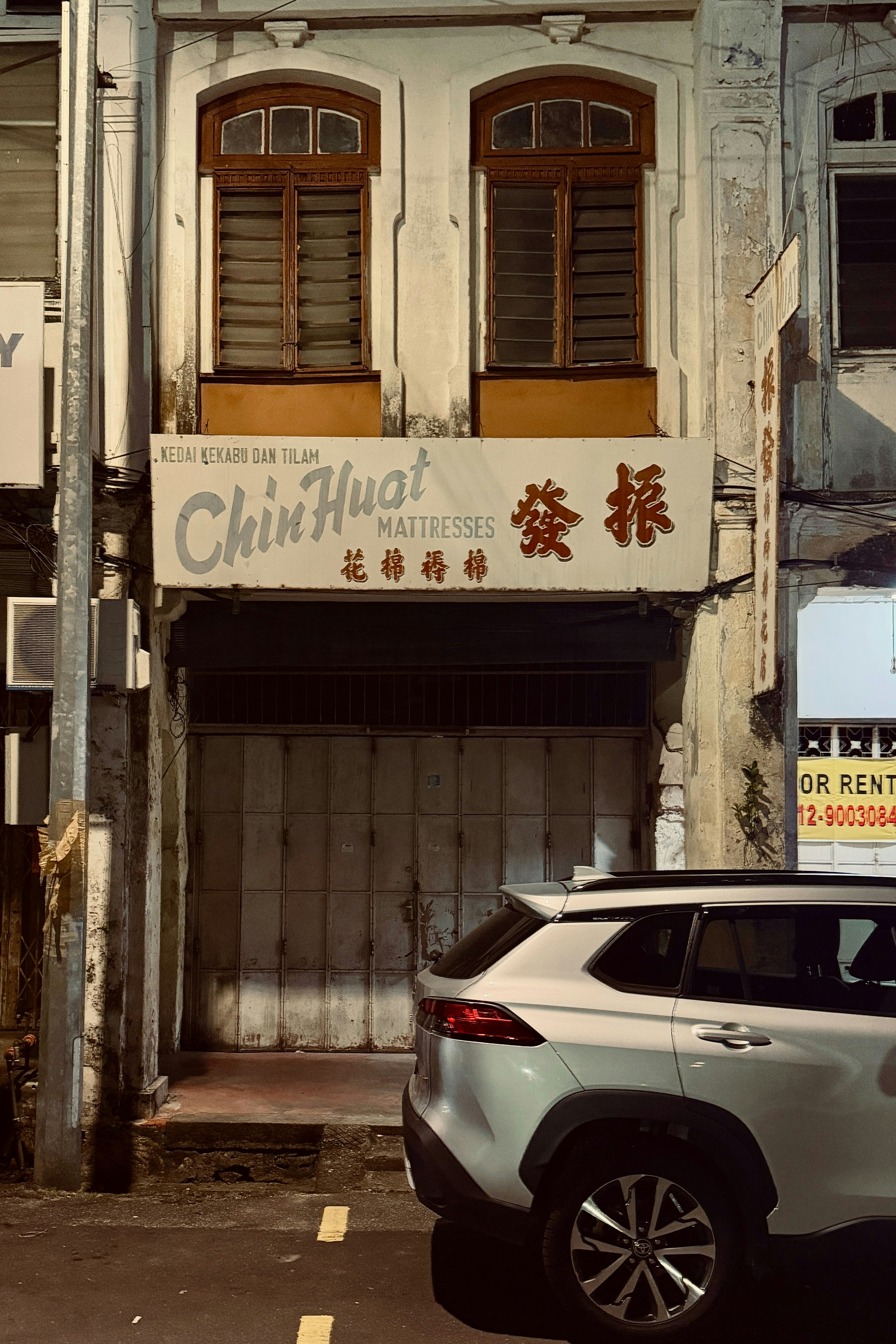 Old storefront with closed shutters and a car.