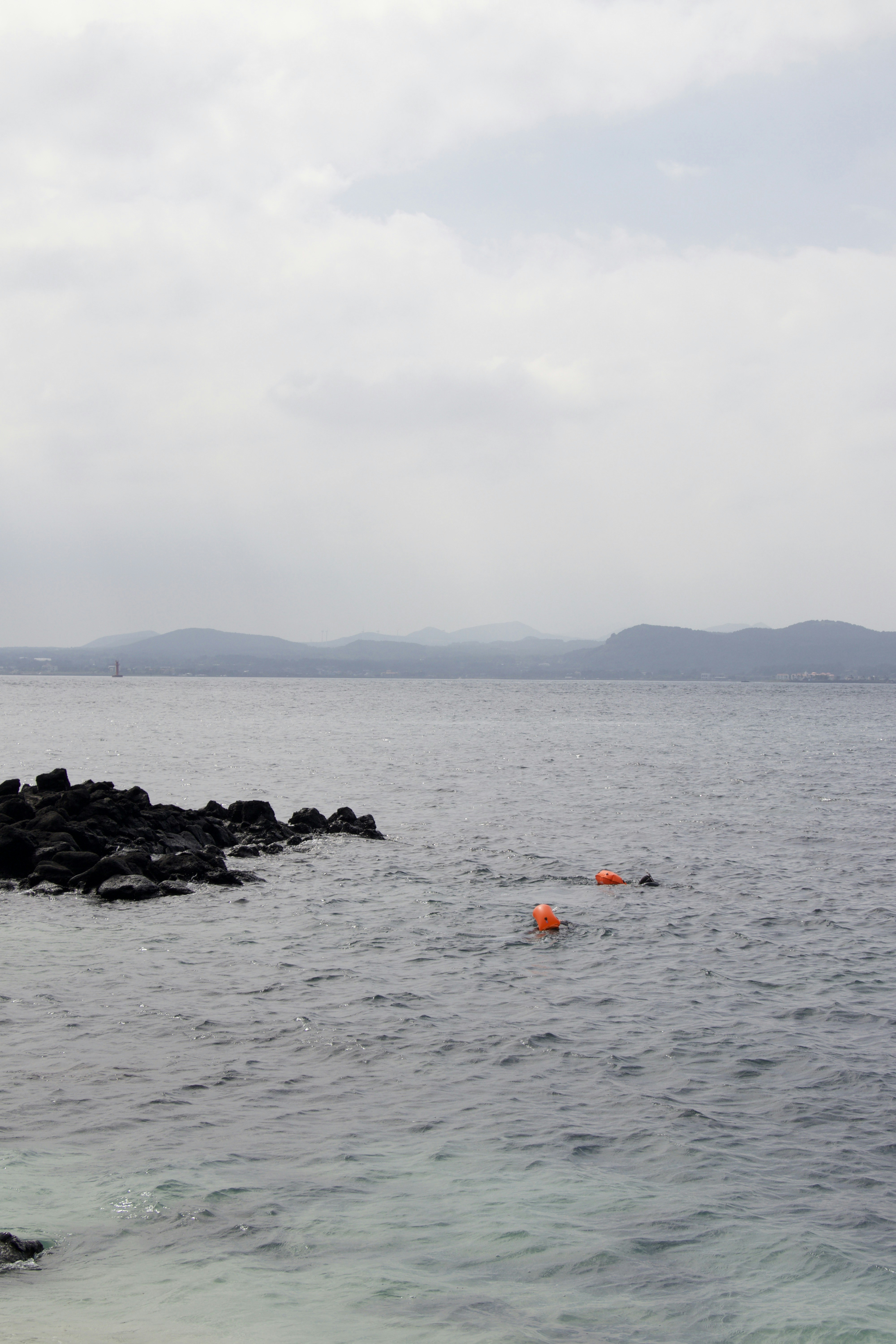 Orange buoys float on the calm ocean near rocky shore.