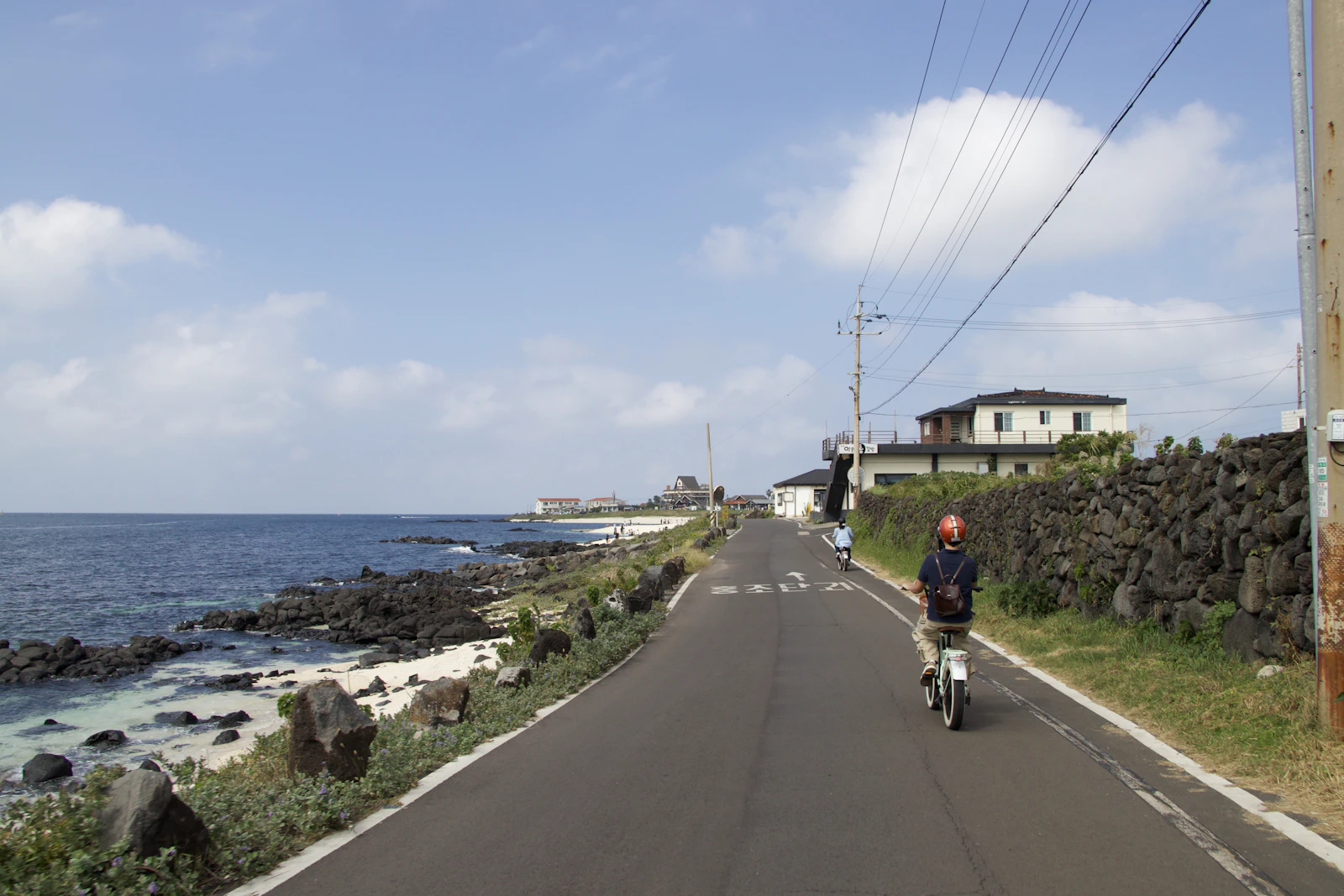 A rider travelling beside black basalt walls on a Jeju coastal road