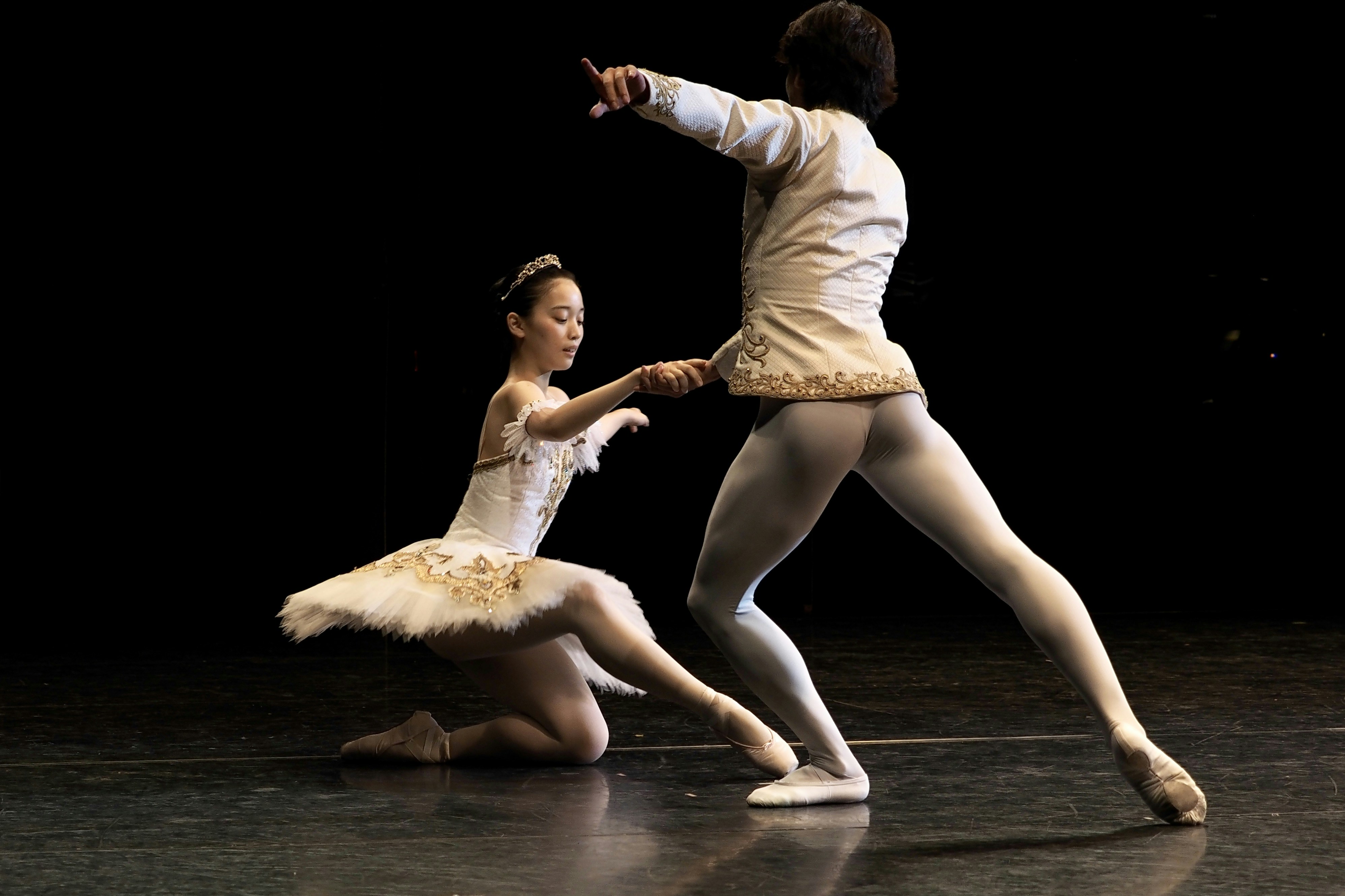 Ballerinas in weißen Kostümen treten auf einer dunklen Bühne auf.