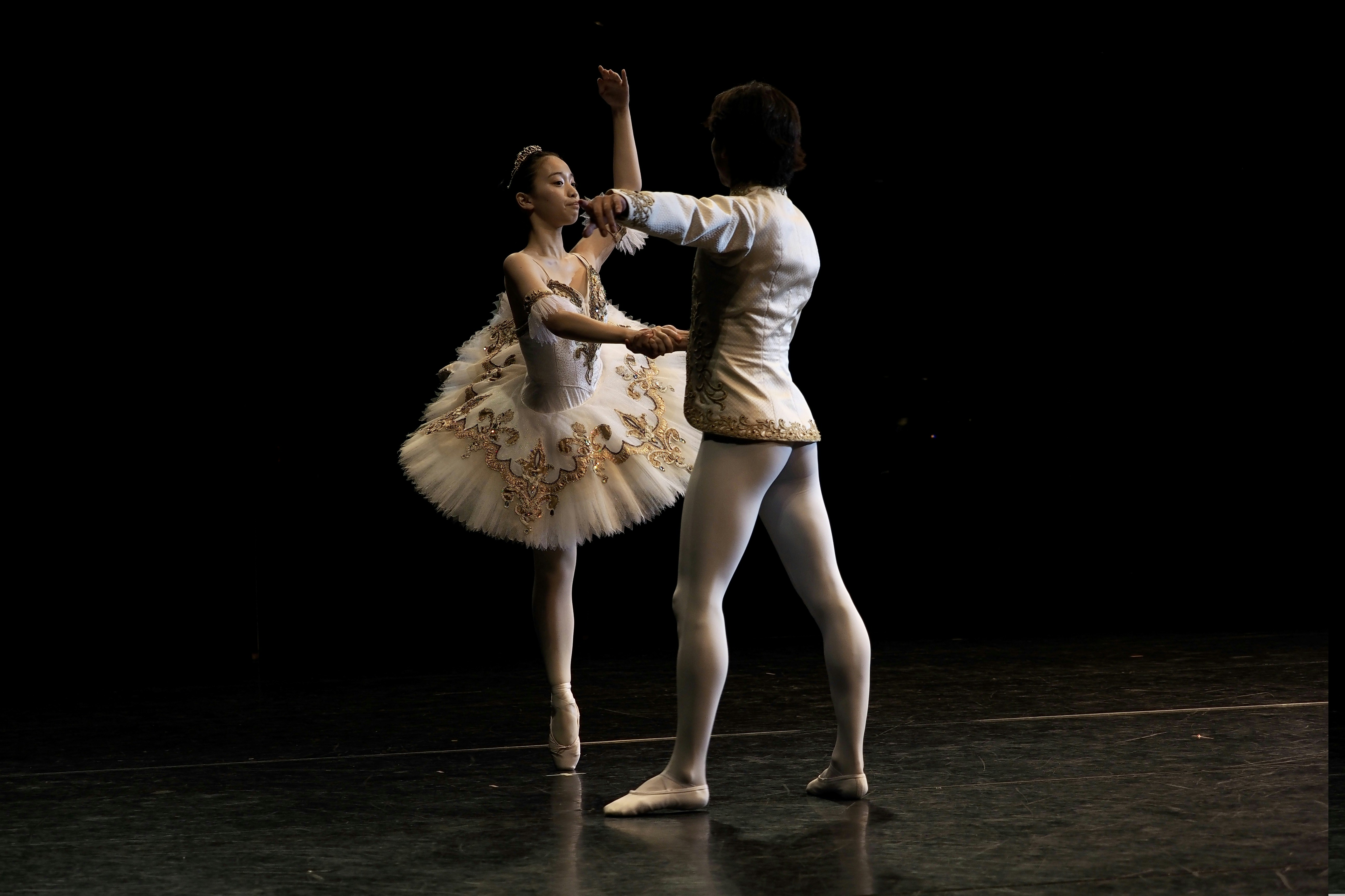 Zwei Balletttänzer treten auf einer dunklen Bühne auf.