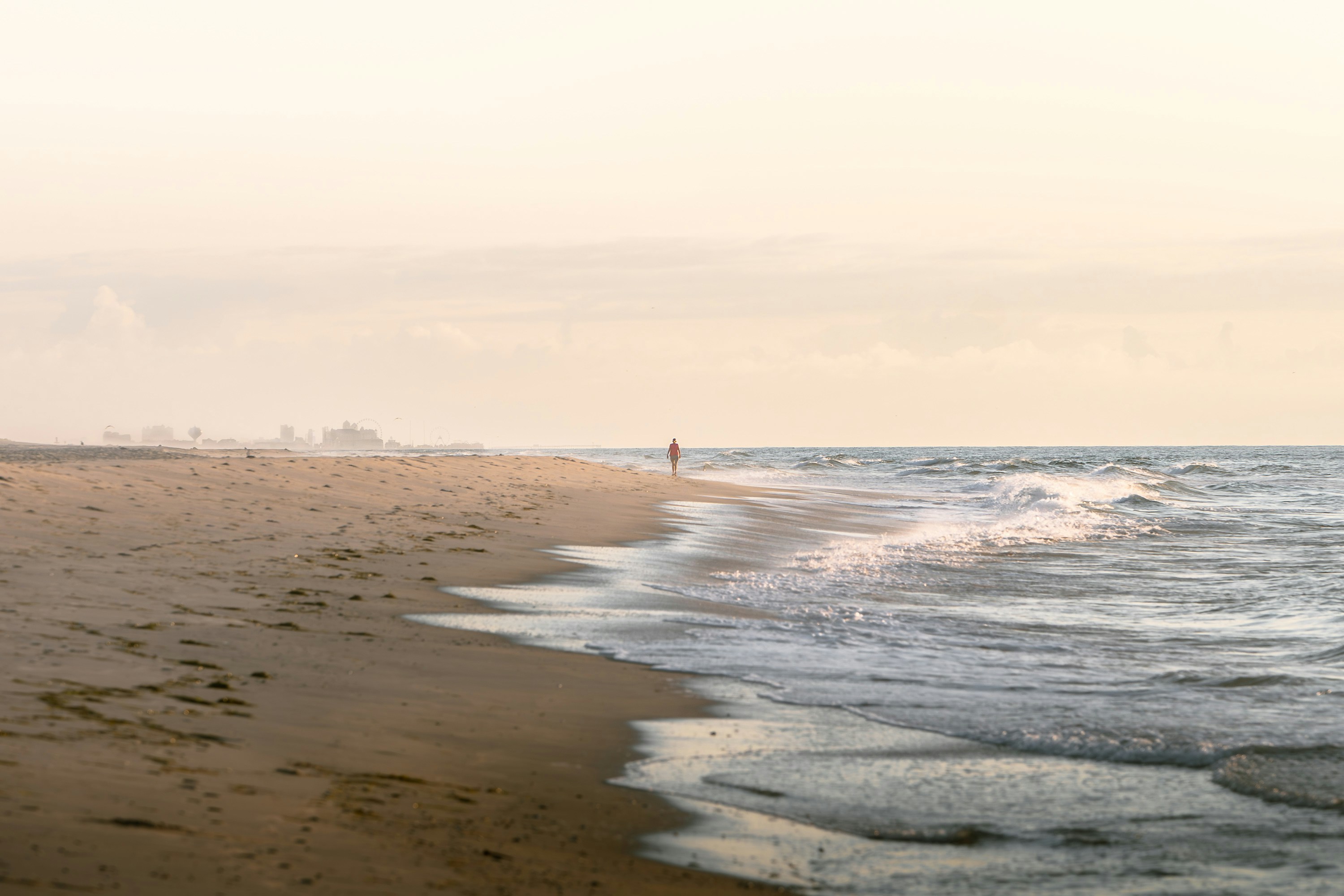Lone figure walks on a sandy beach by the ocean.
