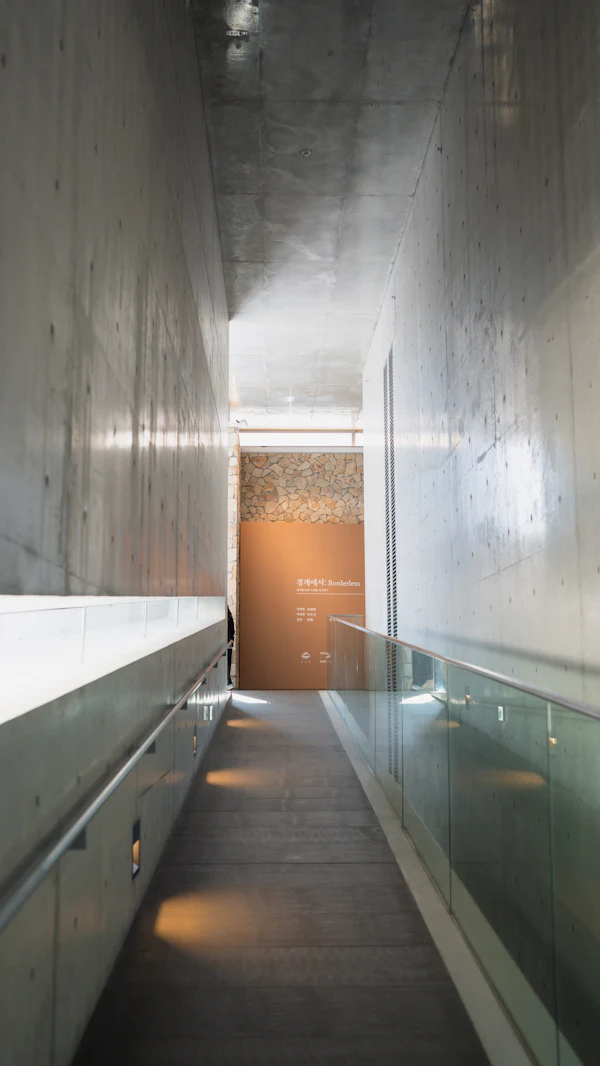 A quiet concrete corridor with a glass balustrade and warm downlights