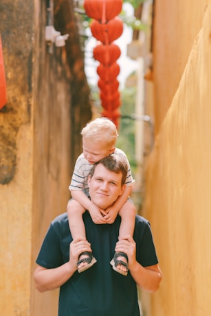 Father carrying his son on his shoulders in alley.