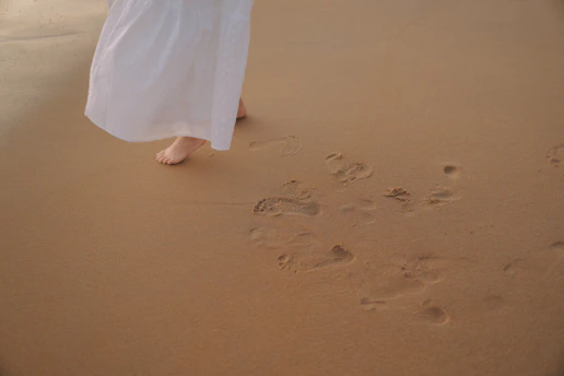 Bare feet walking on a sandy beach leaving footprints.