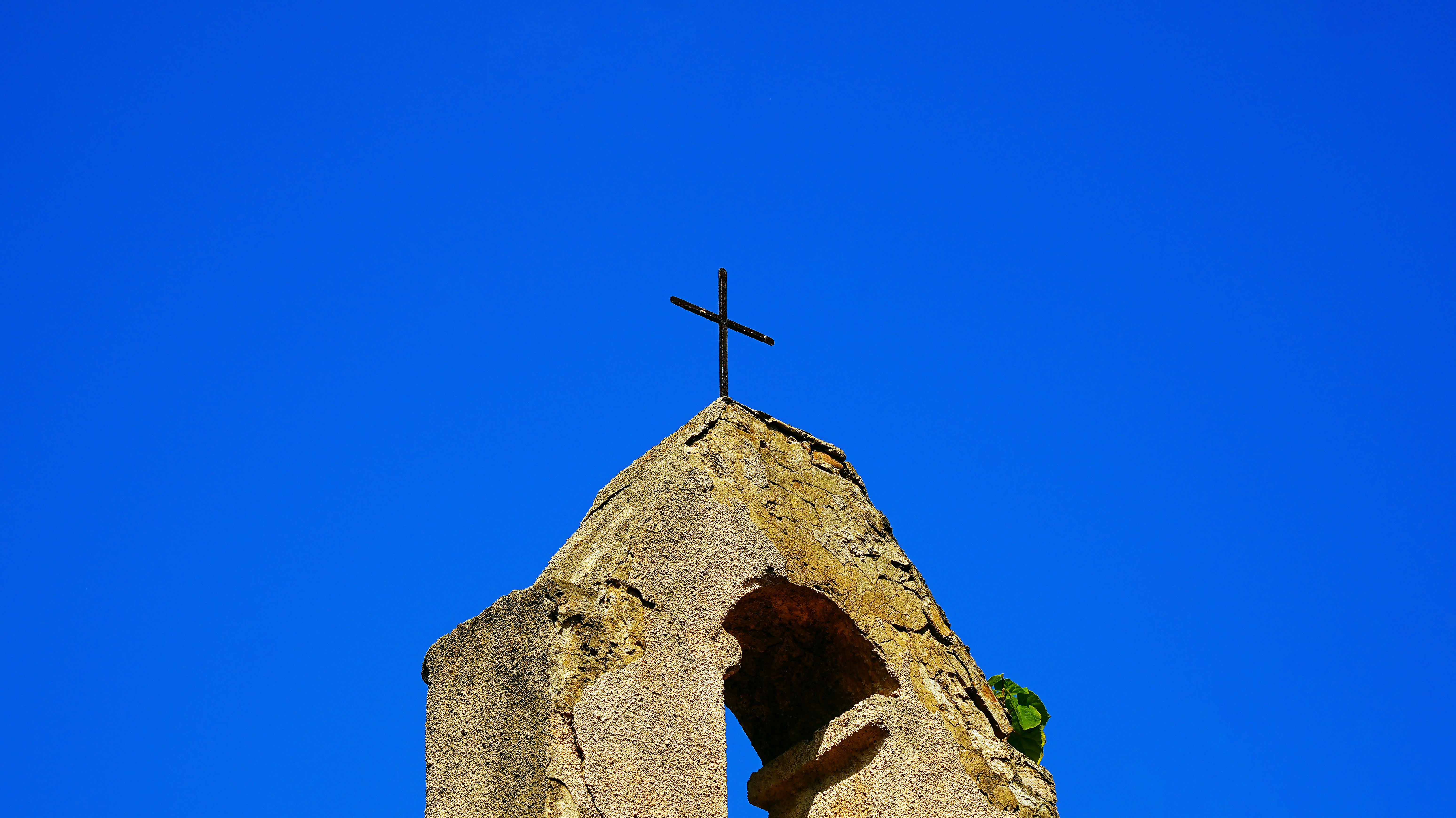 A stone cross atop an old church against blue sky