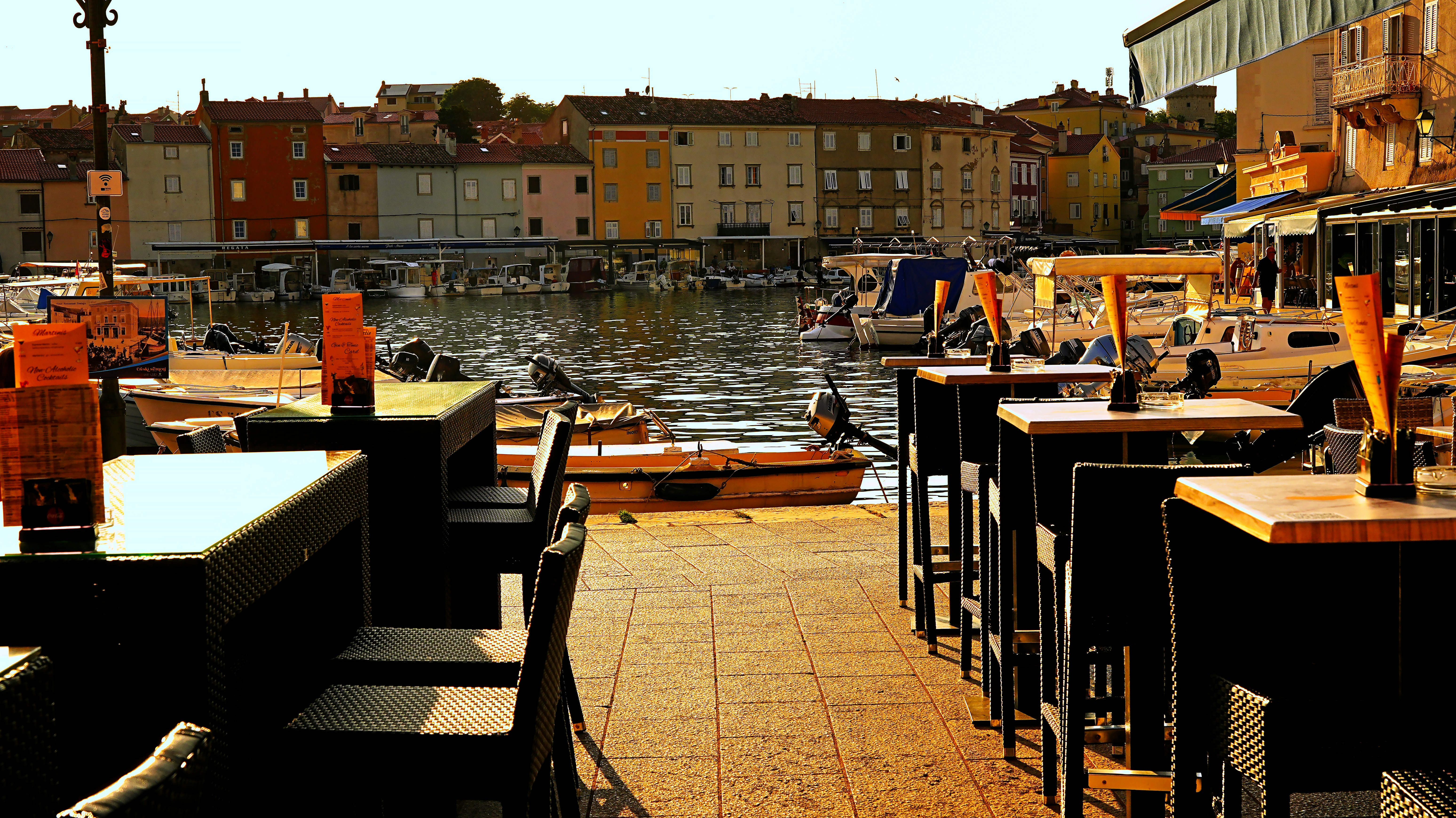 Outdoor cafe tables by a waterfront with buildings.