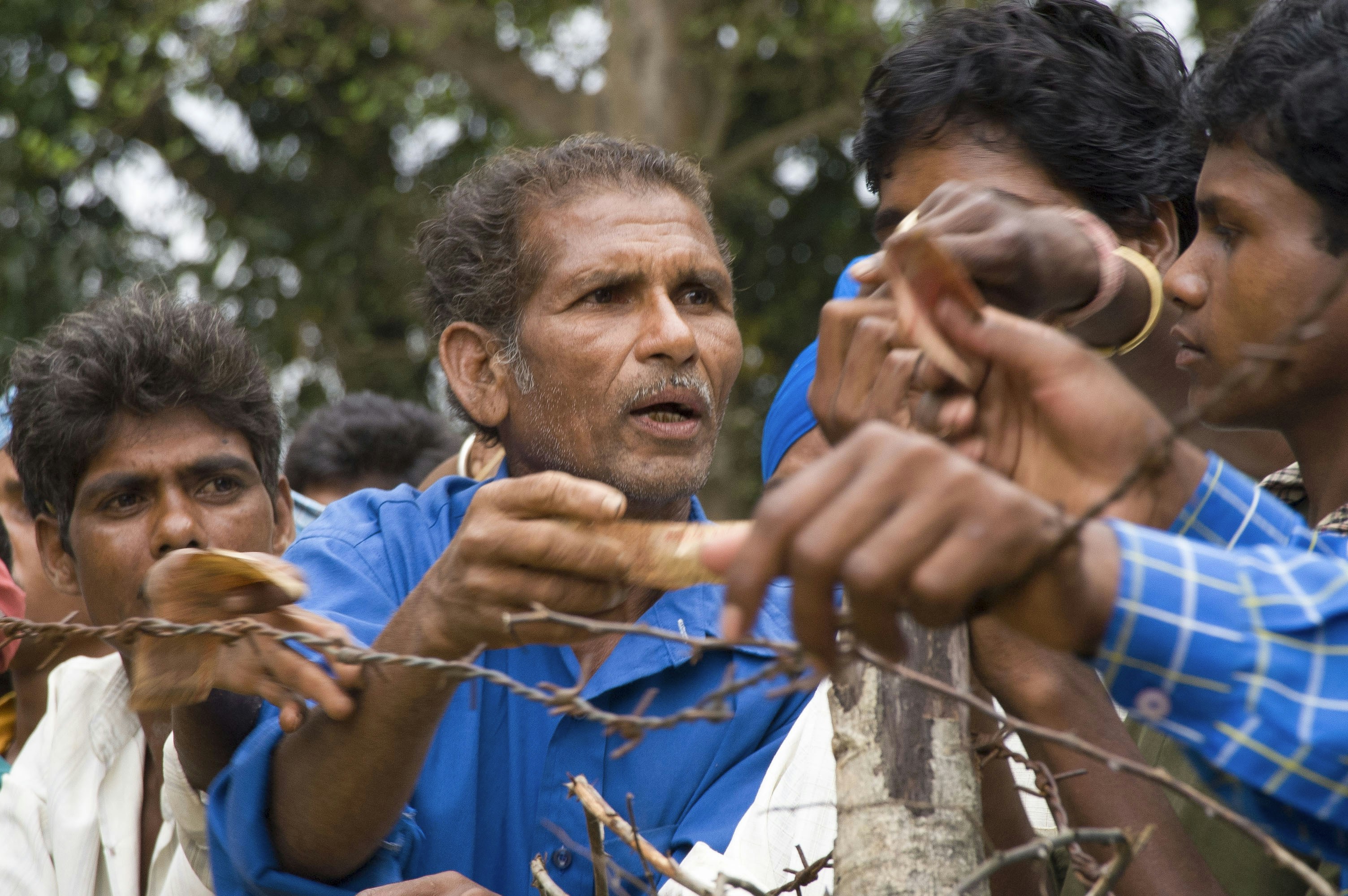 Men gathered behind a barbed wire fence.