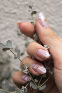 Mano femenina con uñas decoradas sosteniendo planta delicada.