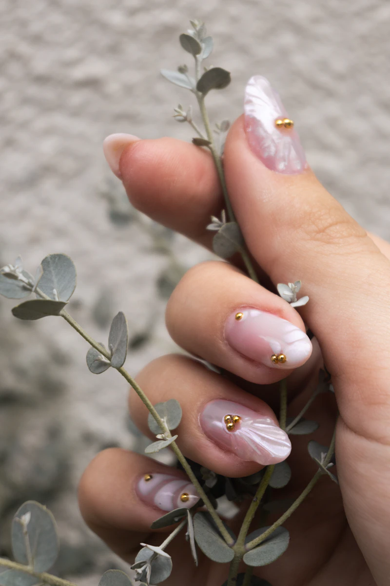 Hand mit rosé-weißer Nail-Art hält einen Eukalyptuszweig