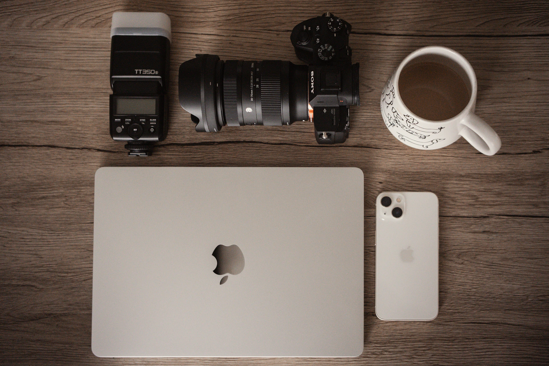 Camera, laptop, phone, and coffee on wooden table