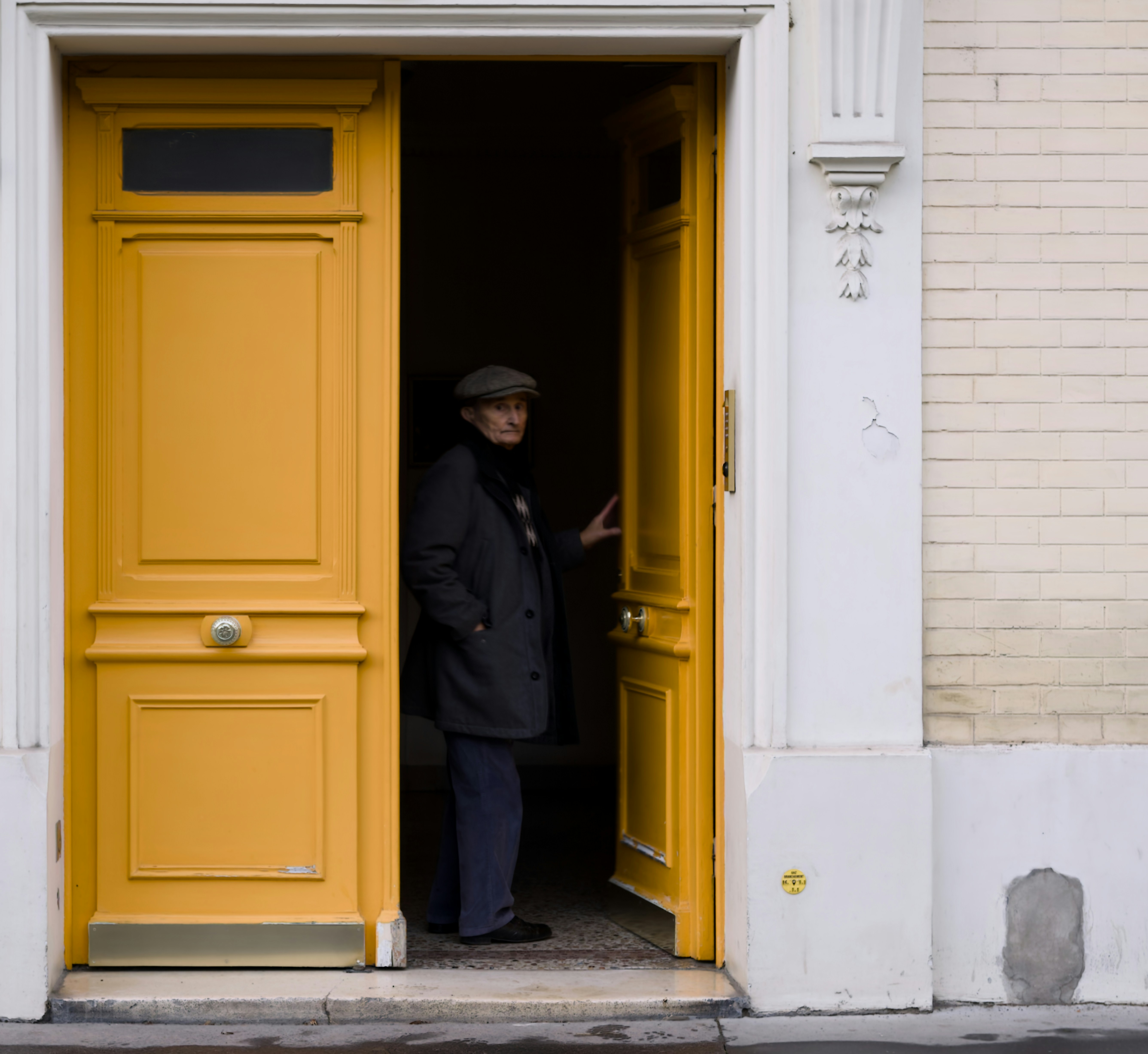 Man in a cap stands in a bright yellow doorway.