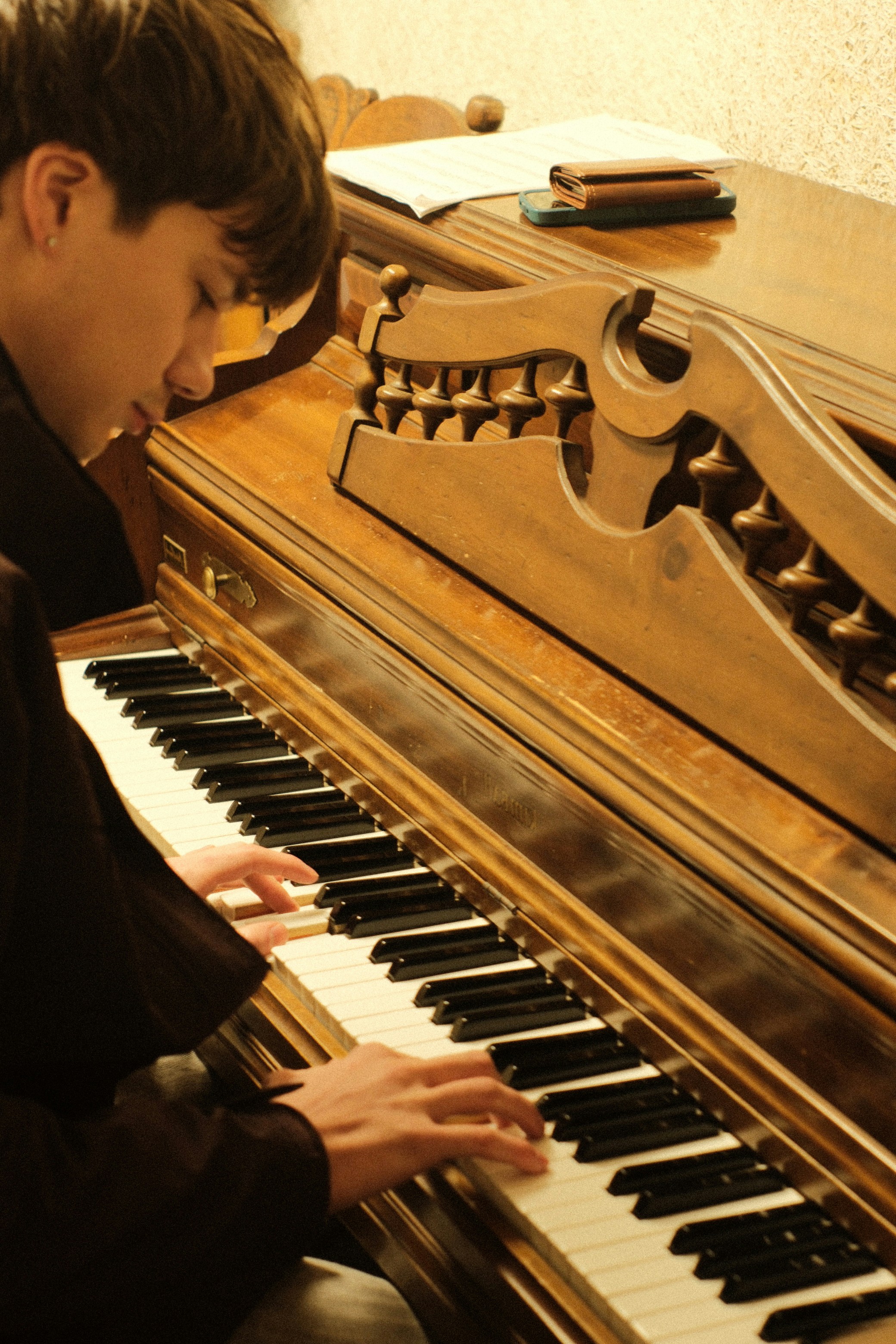 A young person plays a vintage piano with ornate carvings.